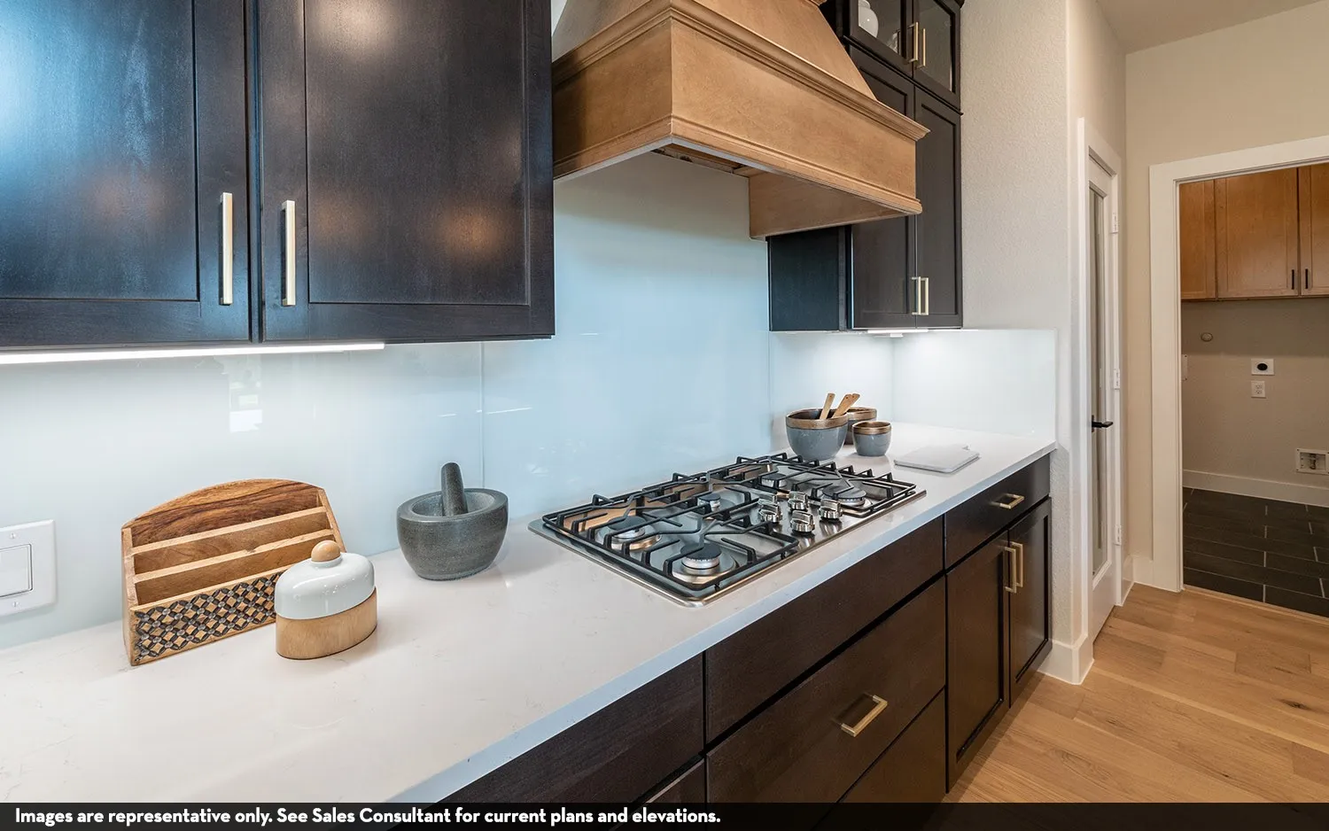 Built-in gas cooktop, wood-finish range hood, dark wood-finish cabinetry, white countertop, and under-cabinet lighting