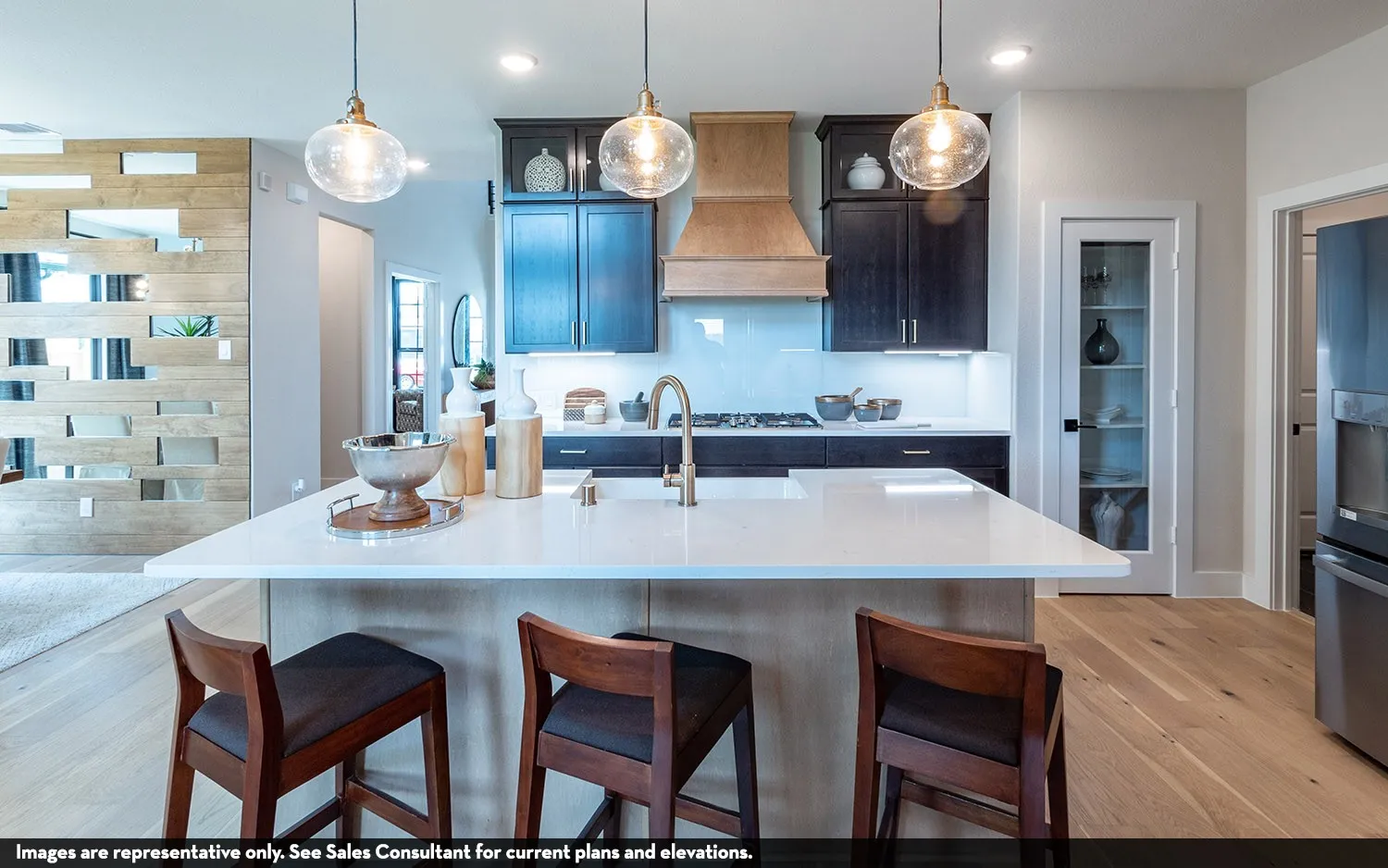 Kitchen featuring a large island with a light-toned countertop, wood-finish flooring, dark cabinetry, and three pendant light fixtures