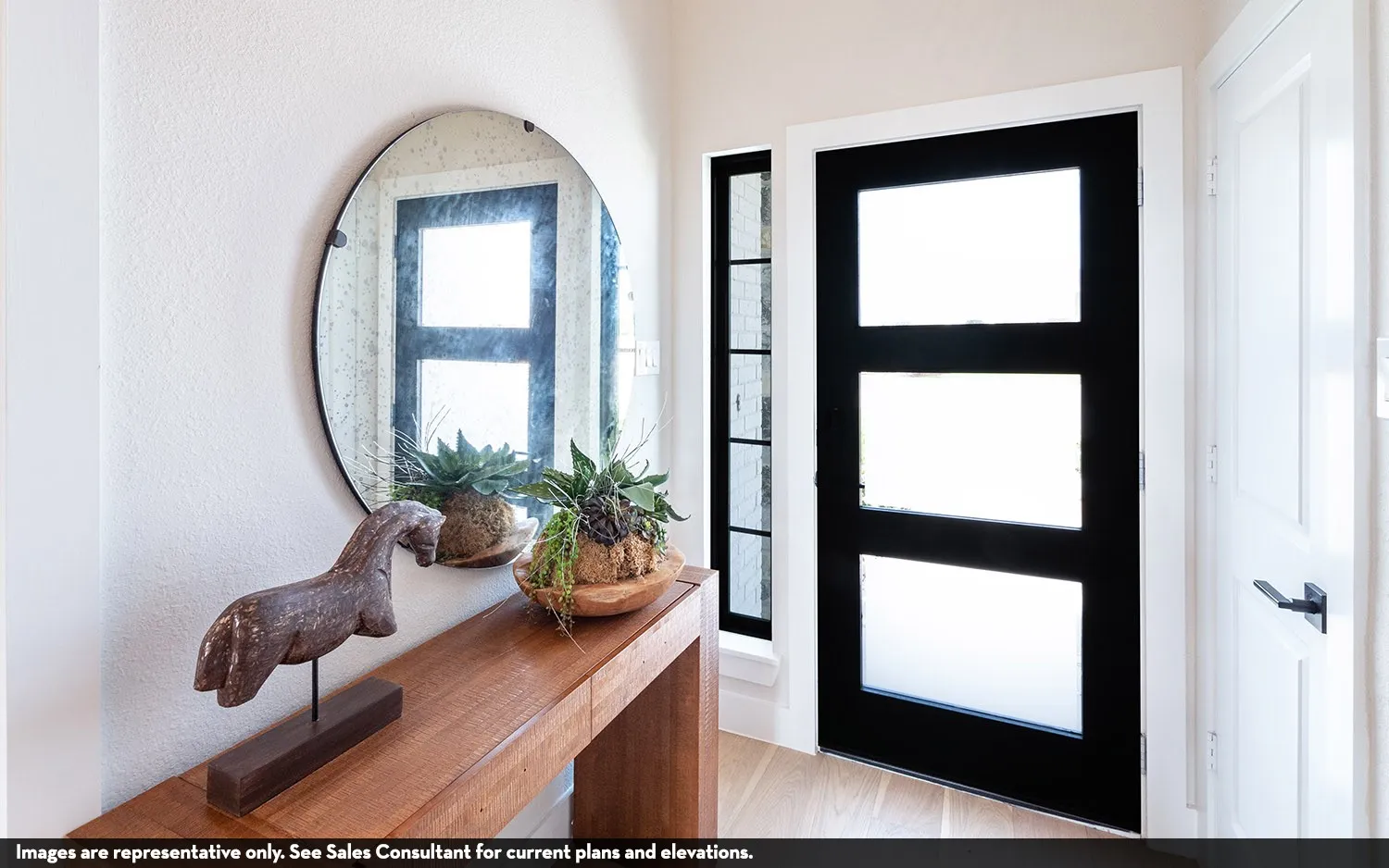 Warm wood-finish console table, round wall-mounted mirror, and sleek black entry door with frosted glass panels