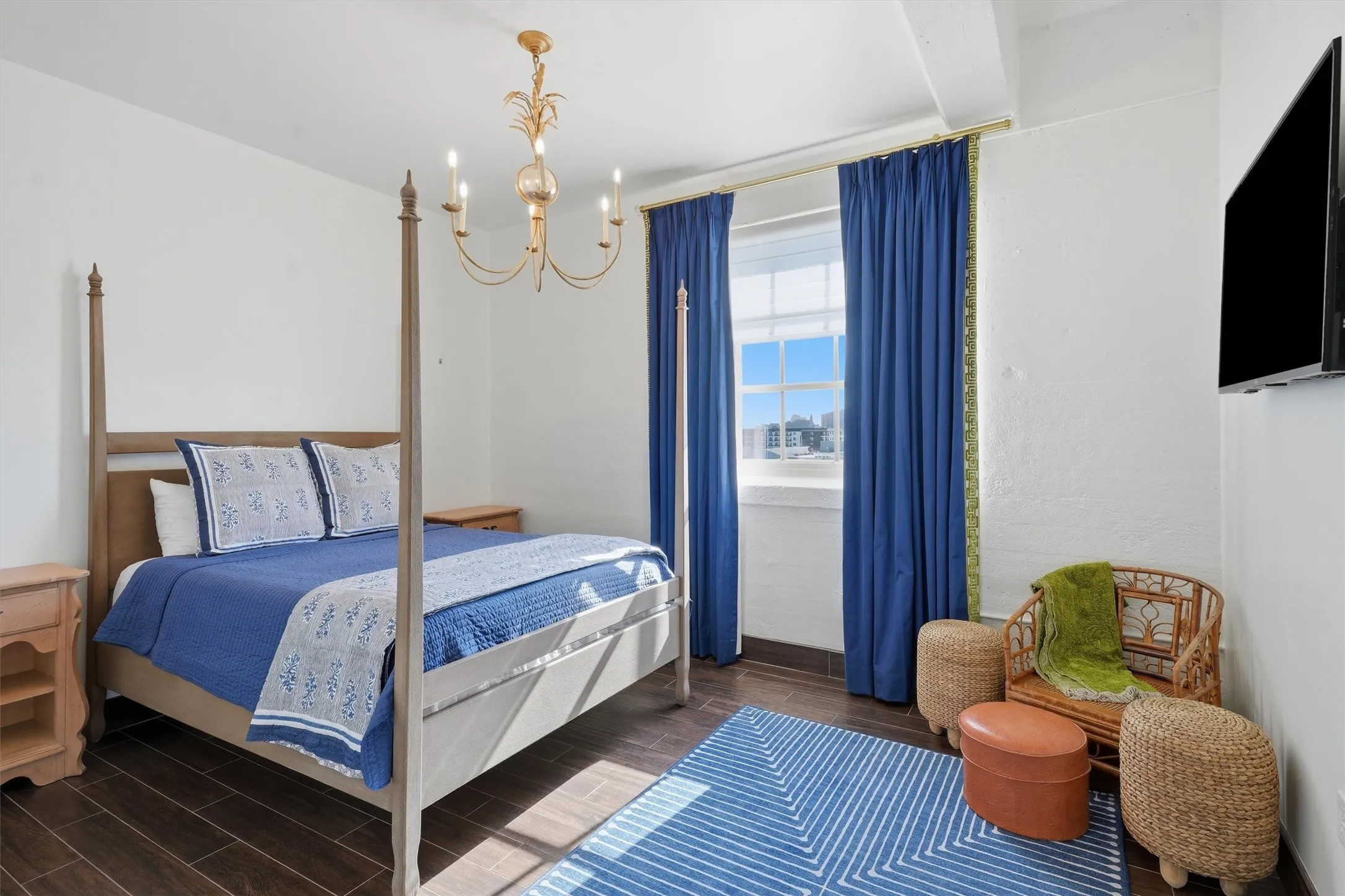 Serene primary bedroom suite featuring high ceilings, a chic gold candle-style chandelier, and bright window views.