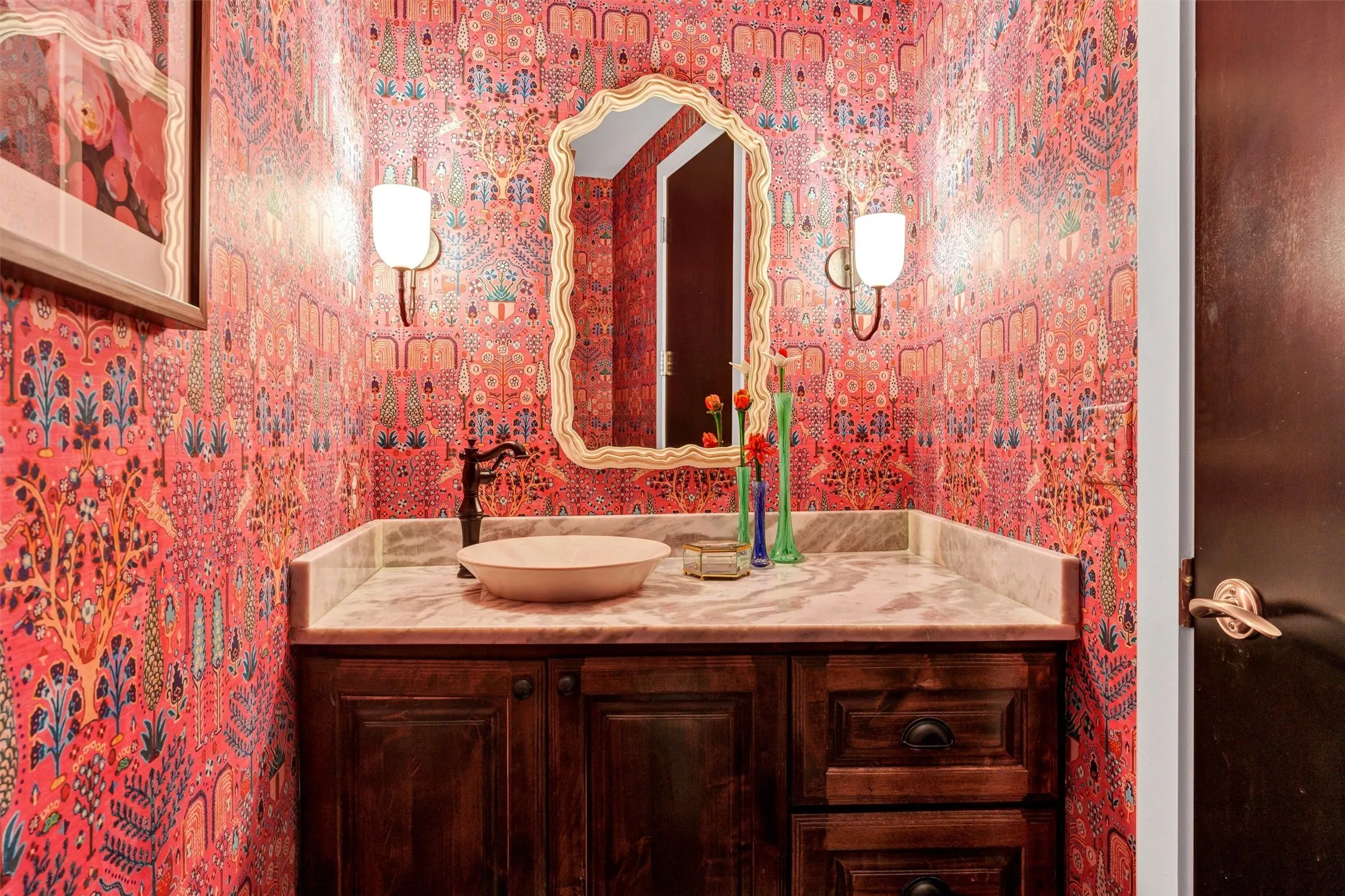 Show-stopping design featuring bold, colorful botanical wallpaper, a wavy scalloped mirror frame, and a sleek marble vanity counter. Conveniently located half-bath for guests.