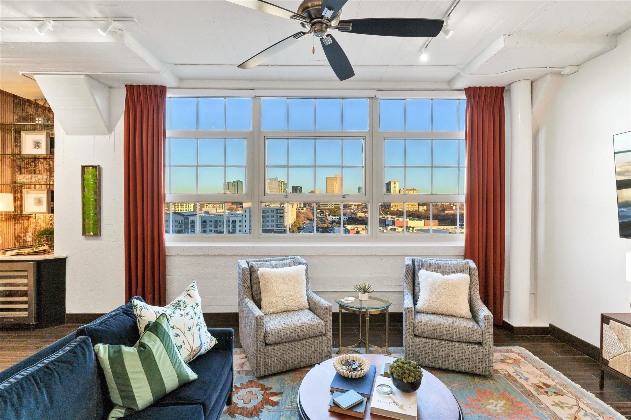 Direct, symmetrical composition showcasing the panoramic downtown view framed by dramatic floor-to-ceiling drapes and industrial architecture.