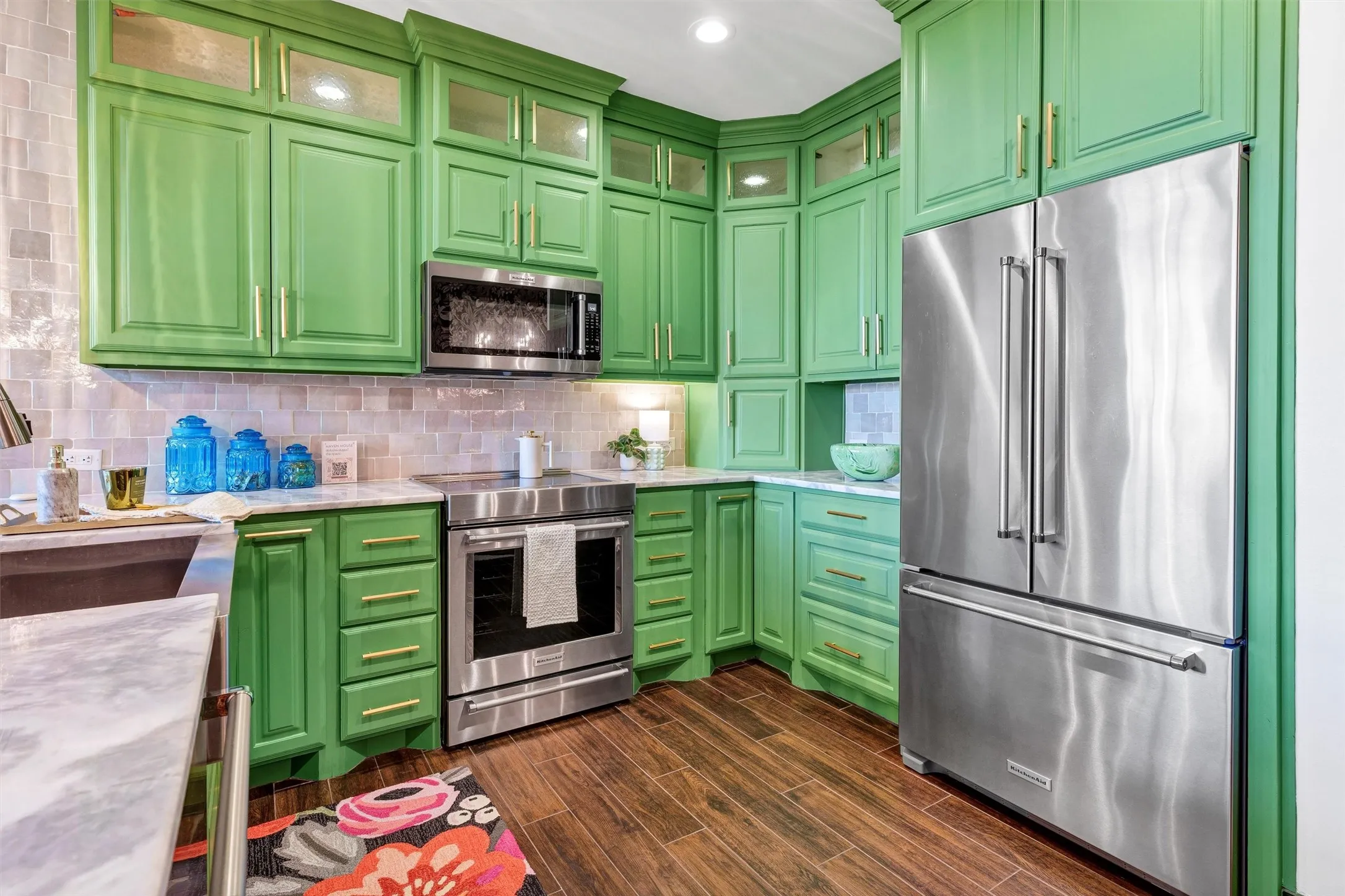 A chef's dream kitchen featuring custom, floor-to-ceiling cabinetry in a vibrant green, anchored by sleek stainless steel appliances. Ample counter space and integrated storage, including upper glass-front cabinets, offer both form and functional workspace.