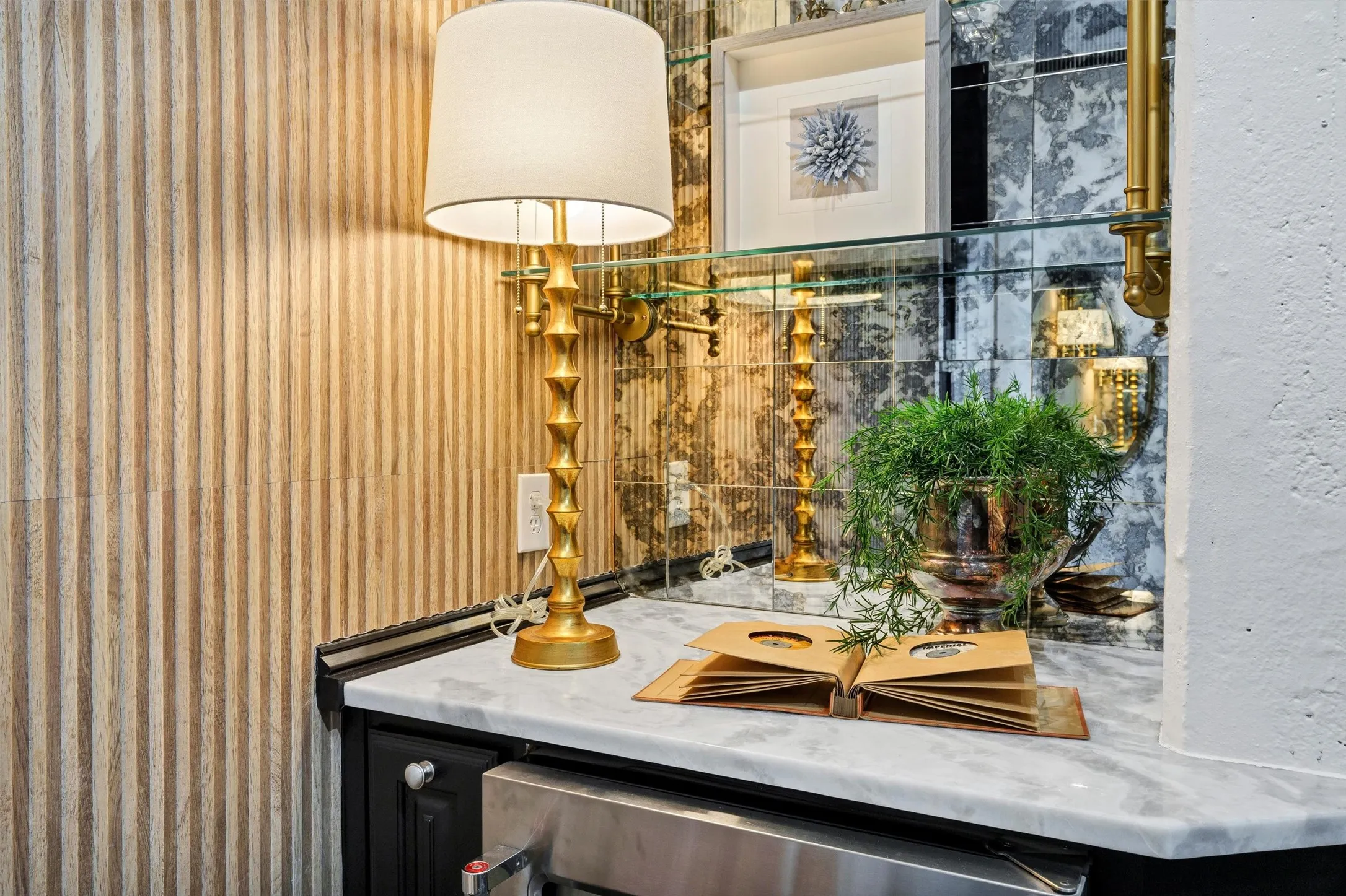 Bespoke bar and beverage station featuring marble countertops, antiqued mirror glass tile backsplash, and fluted wood wall accents. Designed with an under-counter beverage fridge and glass shelving for elevated entertaining.