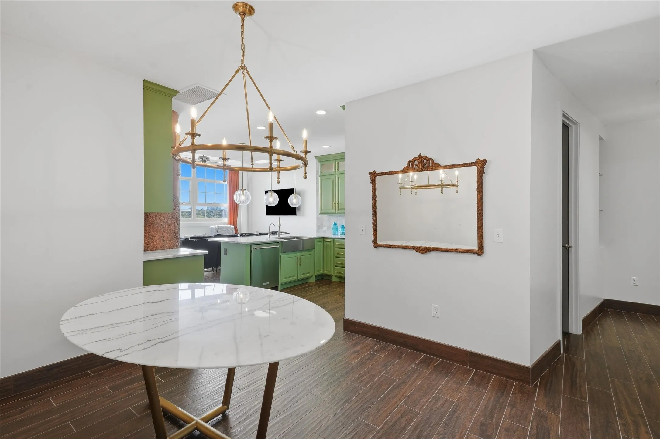 Dedicated dining area anchored by a brass wagon-wheel chandelier, offering sightlines into the main kitchen and living space. Features rich wood-look flooring and an adjacent foyer hallway, creating a warm, defined entry zone.