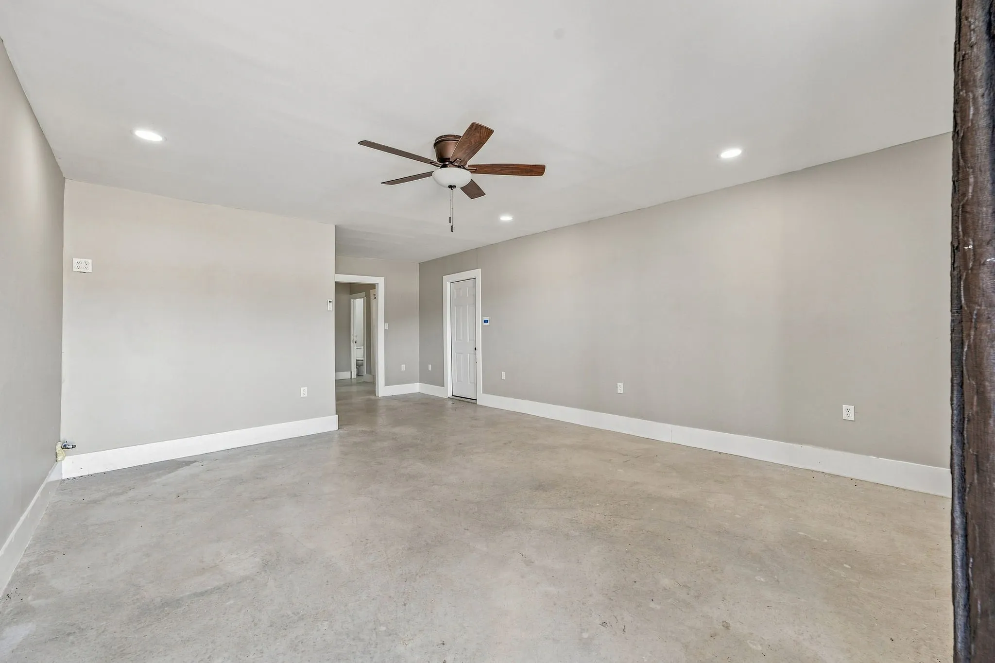 Spacious room featuring concrete flooring, recessed lighting, a ceiling fan, and crisp white trim