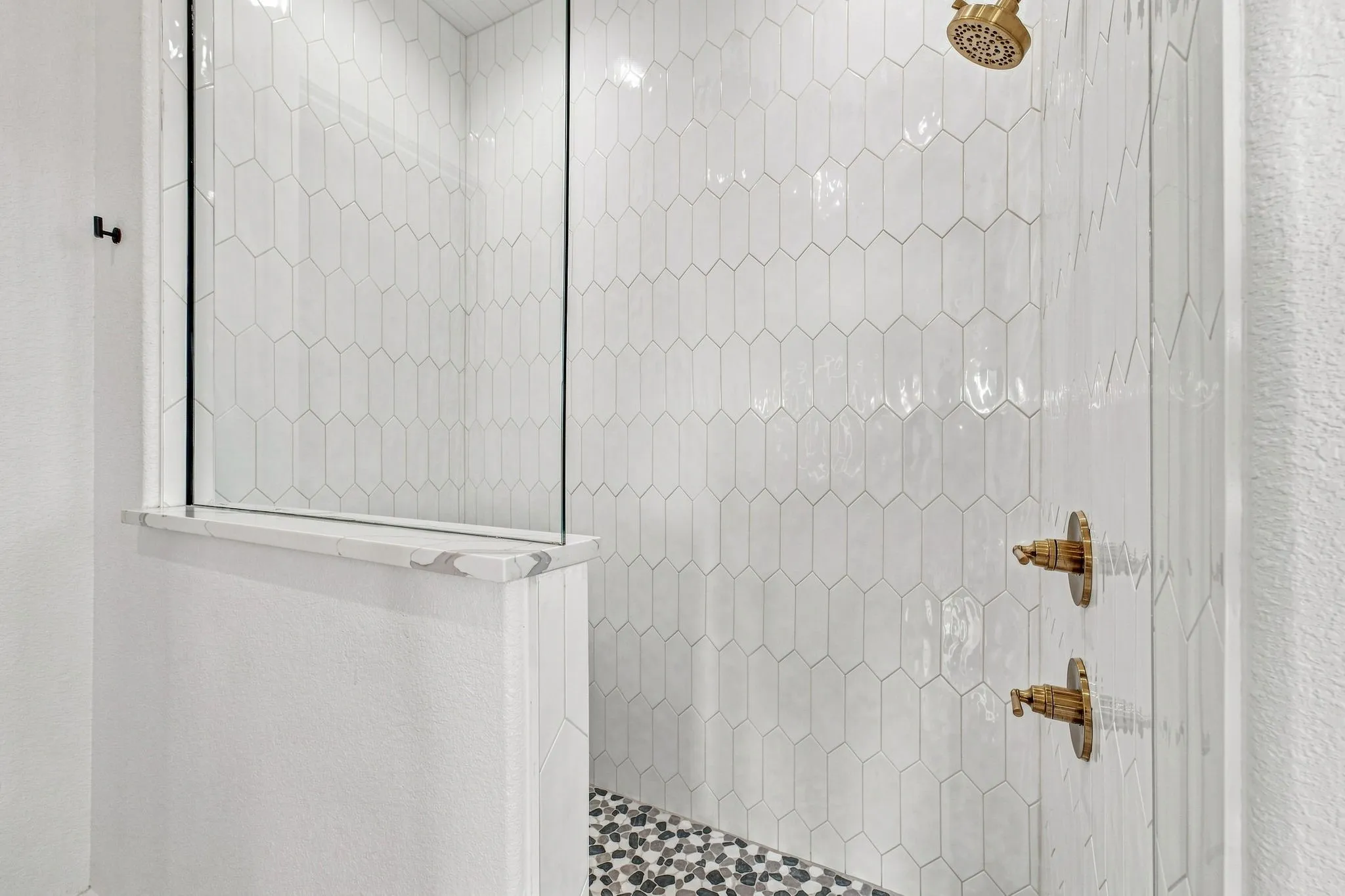 Walk-in shower with vertical picket tile, glass shower enclosure, integrated shower shelf, and gold-finish fixtures