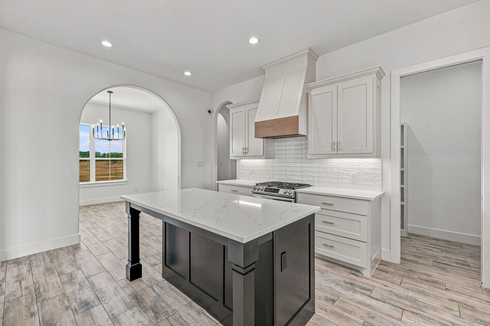 Kitchen featuring a large island with a light-toned countertop, stainless steel range, white cabinetry, and wood-finish flooring