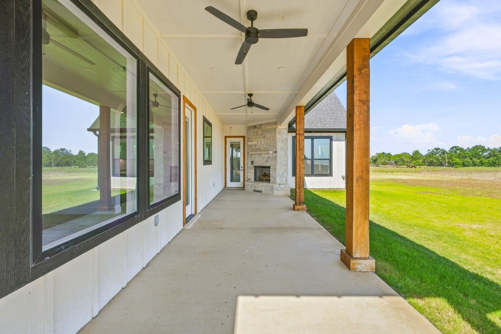Expansive covered patio featuring a stone fireplace, wood support columns, concrete flooring, and ceiling fans