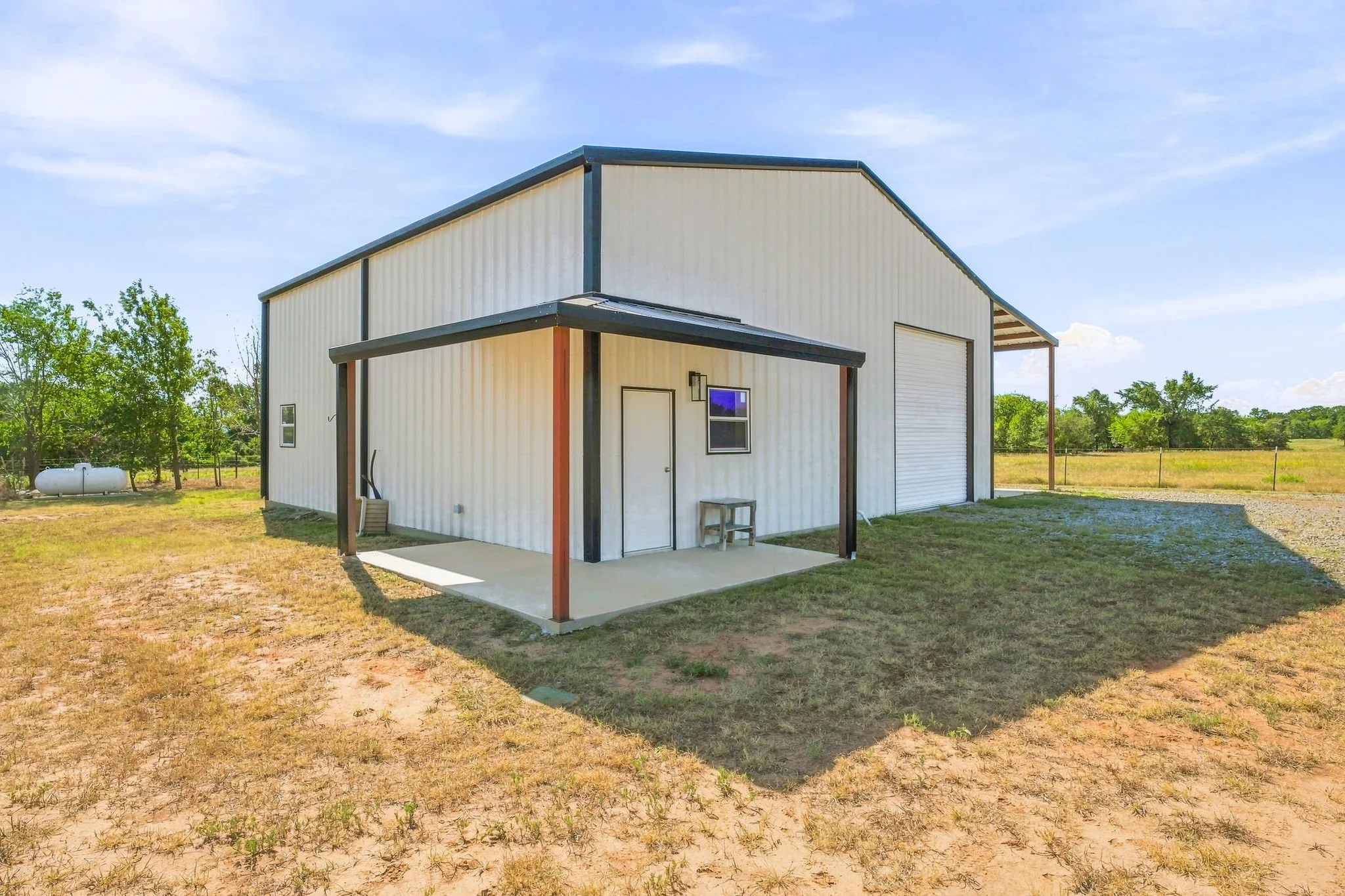 Metal-sided structure featuring a covered concrete patio, a roll-up garage door, and an additional personnel door