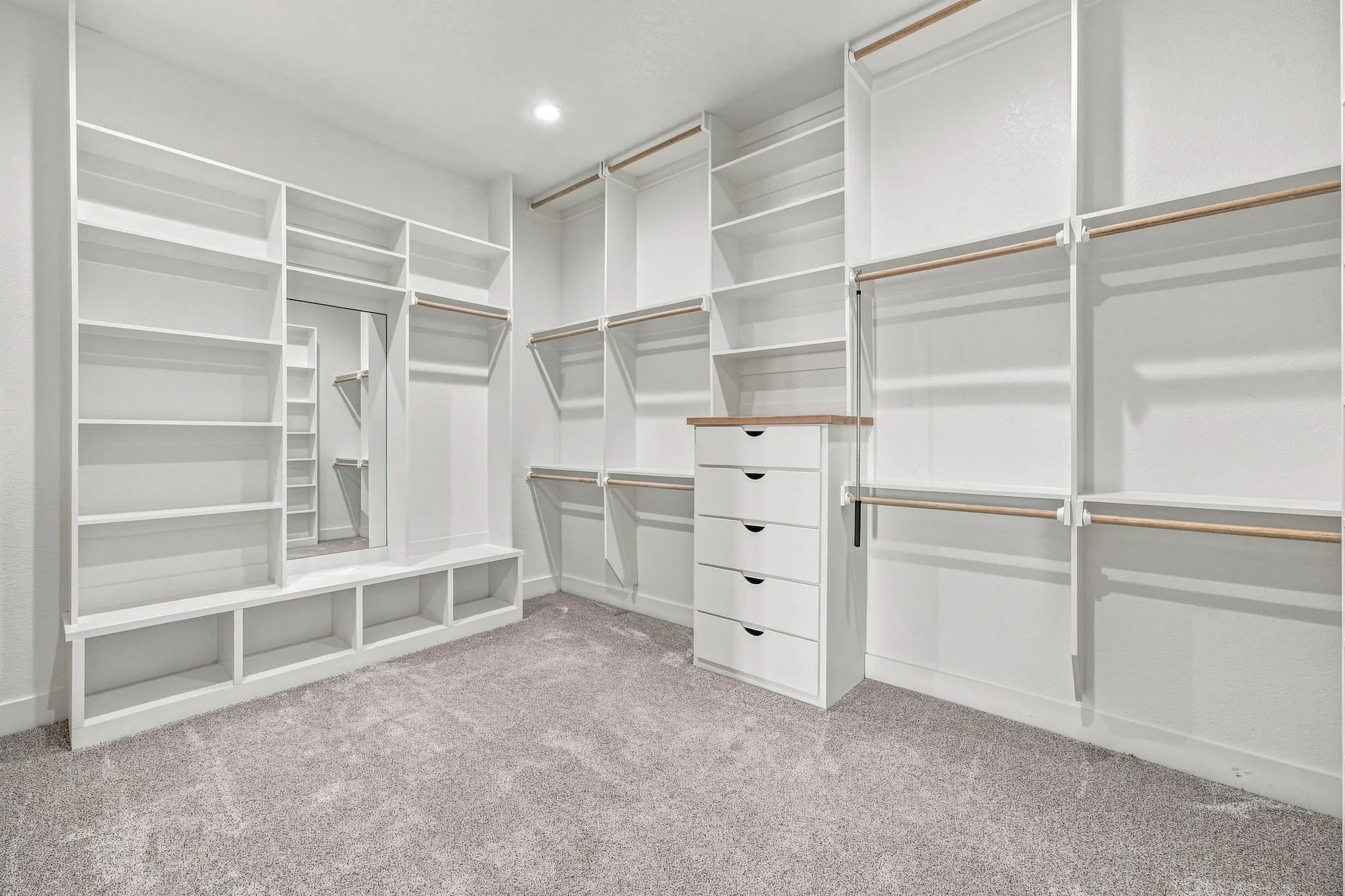 Spacious walk-in closet featuring extensive built-in shelving, hanging rods, an integrated mirror, and a five-drawer dresser with a wood-finish top