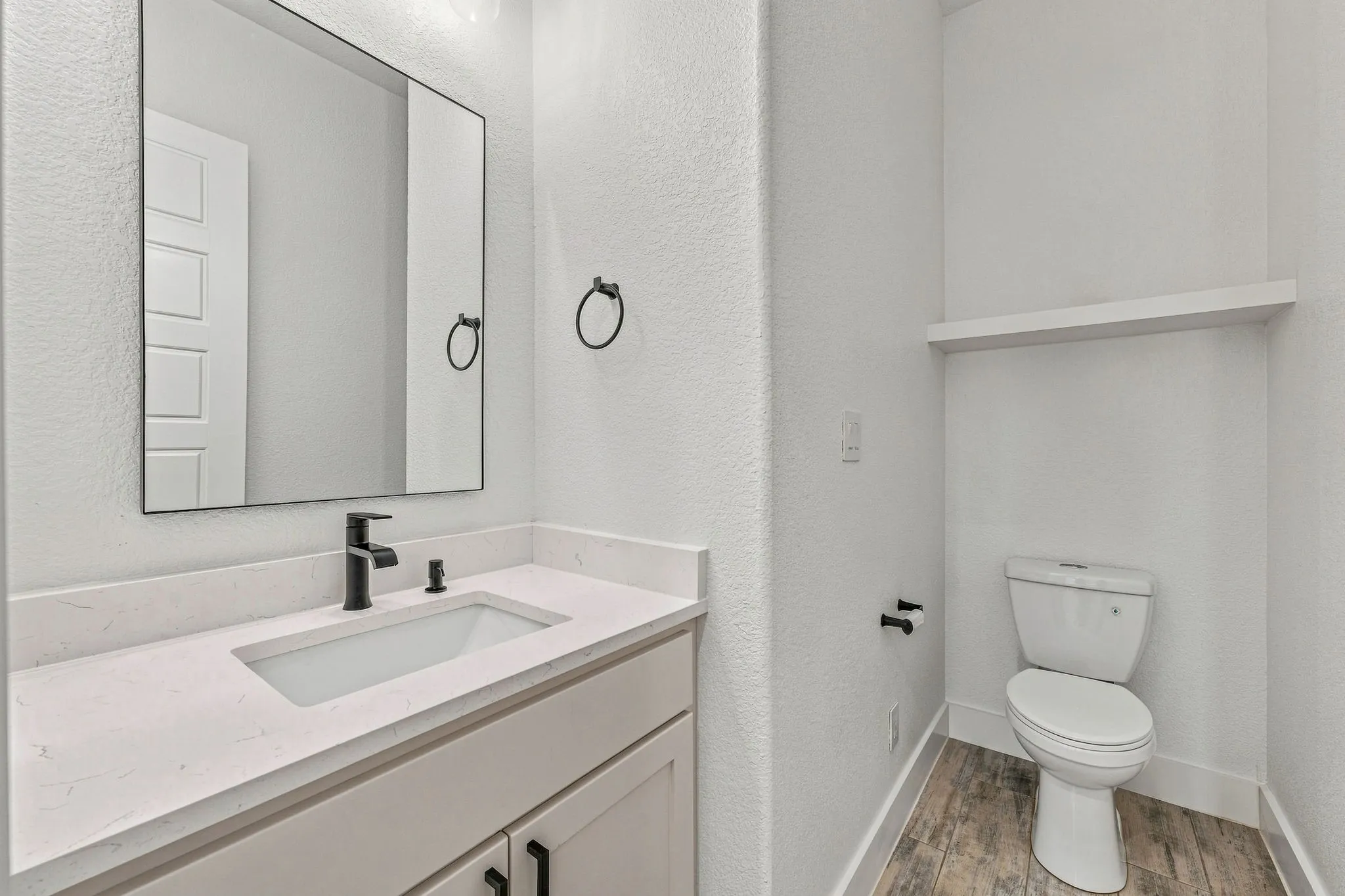 Vanity with integrated rectangular sink, stone-finish countertop, black-finish faucet, and wood-finish flooring