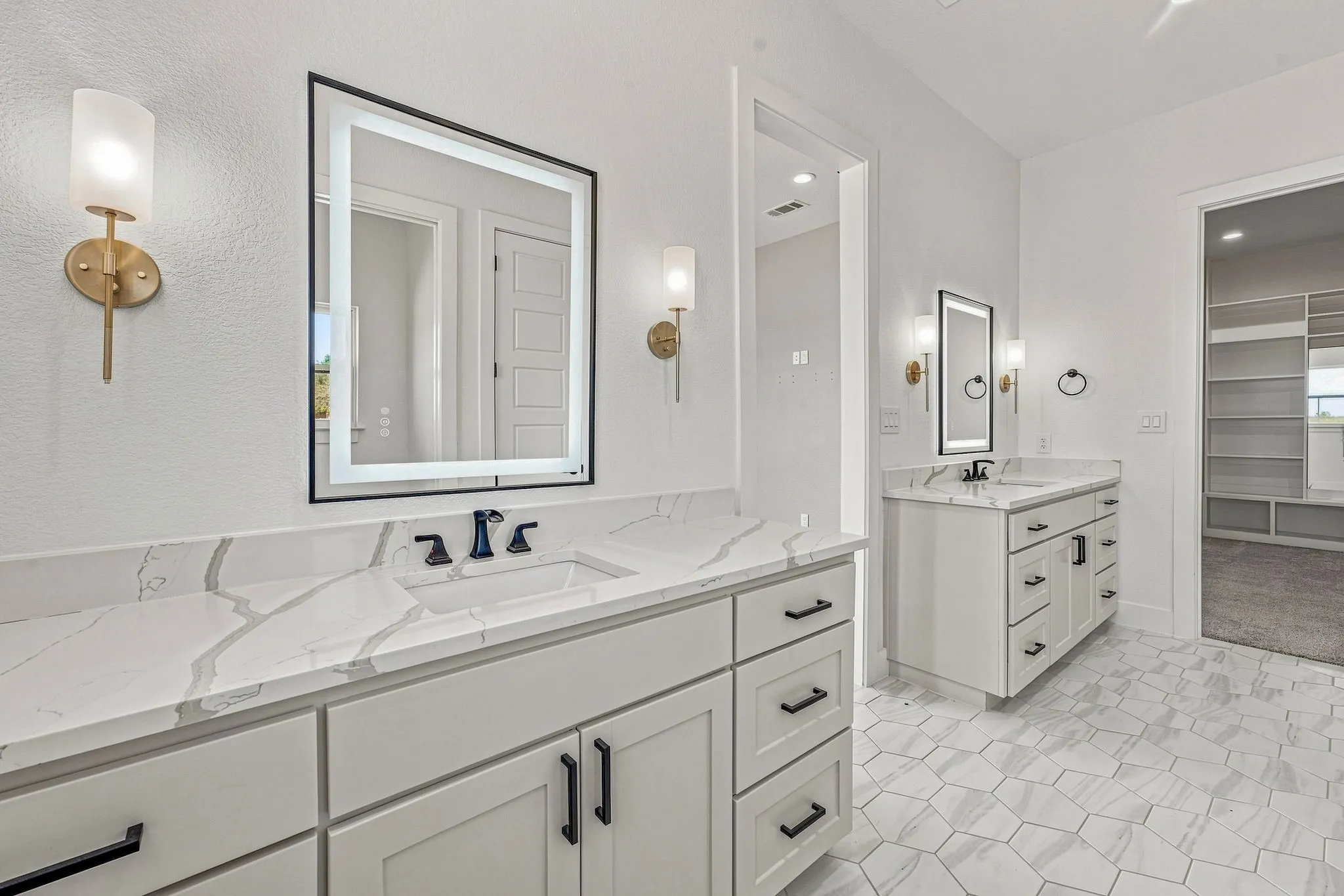 Dual vanities featuring white cabinetry with black hardware, white countertops with veining, and integrated sinks