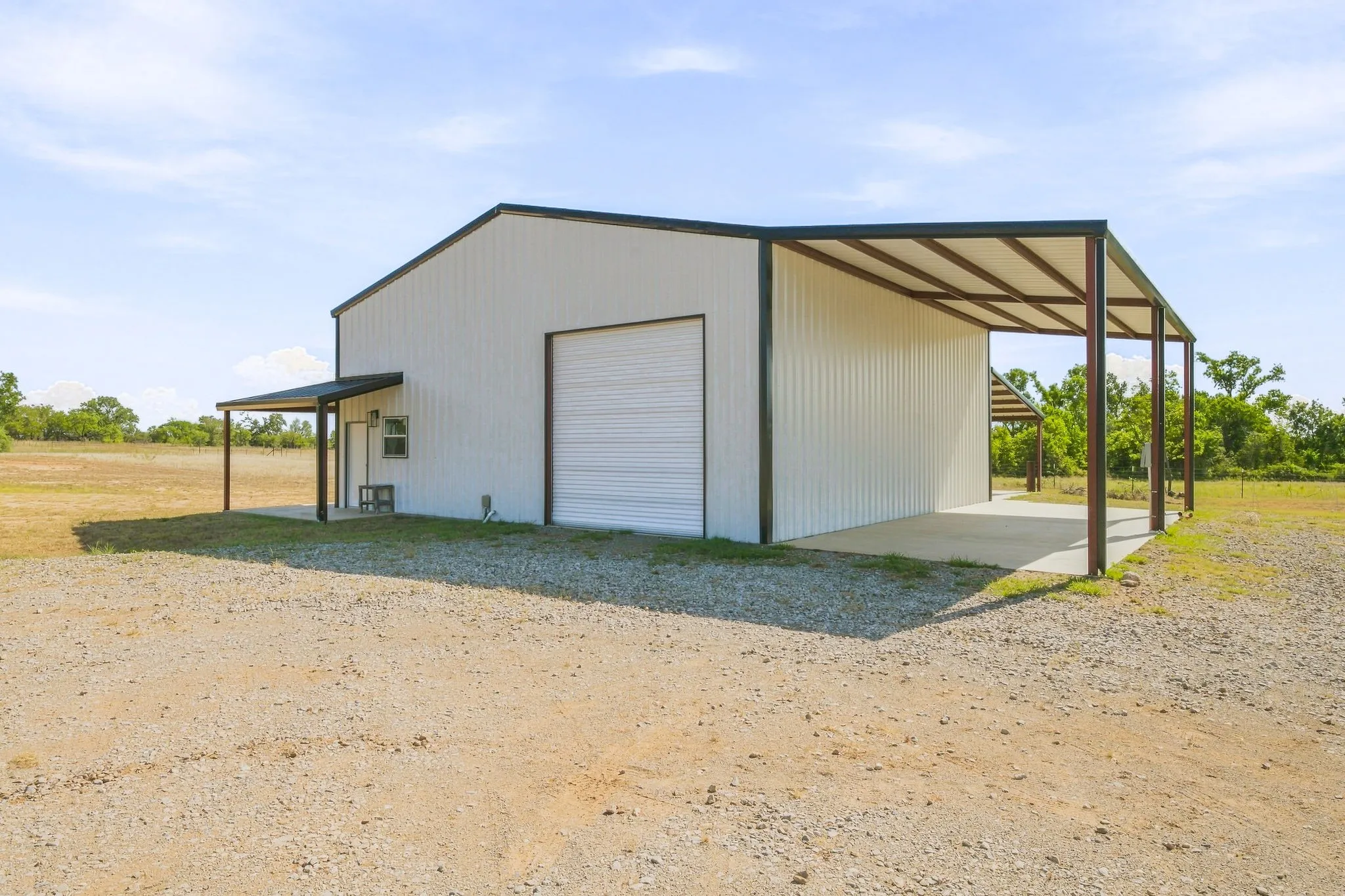 White metal construction with a roll-up door, an attached open-air carport, and a covered entry