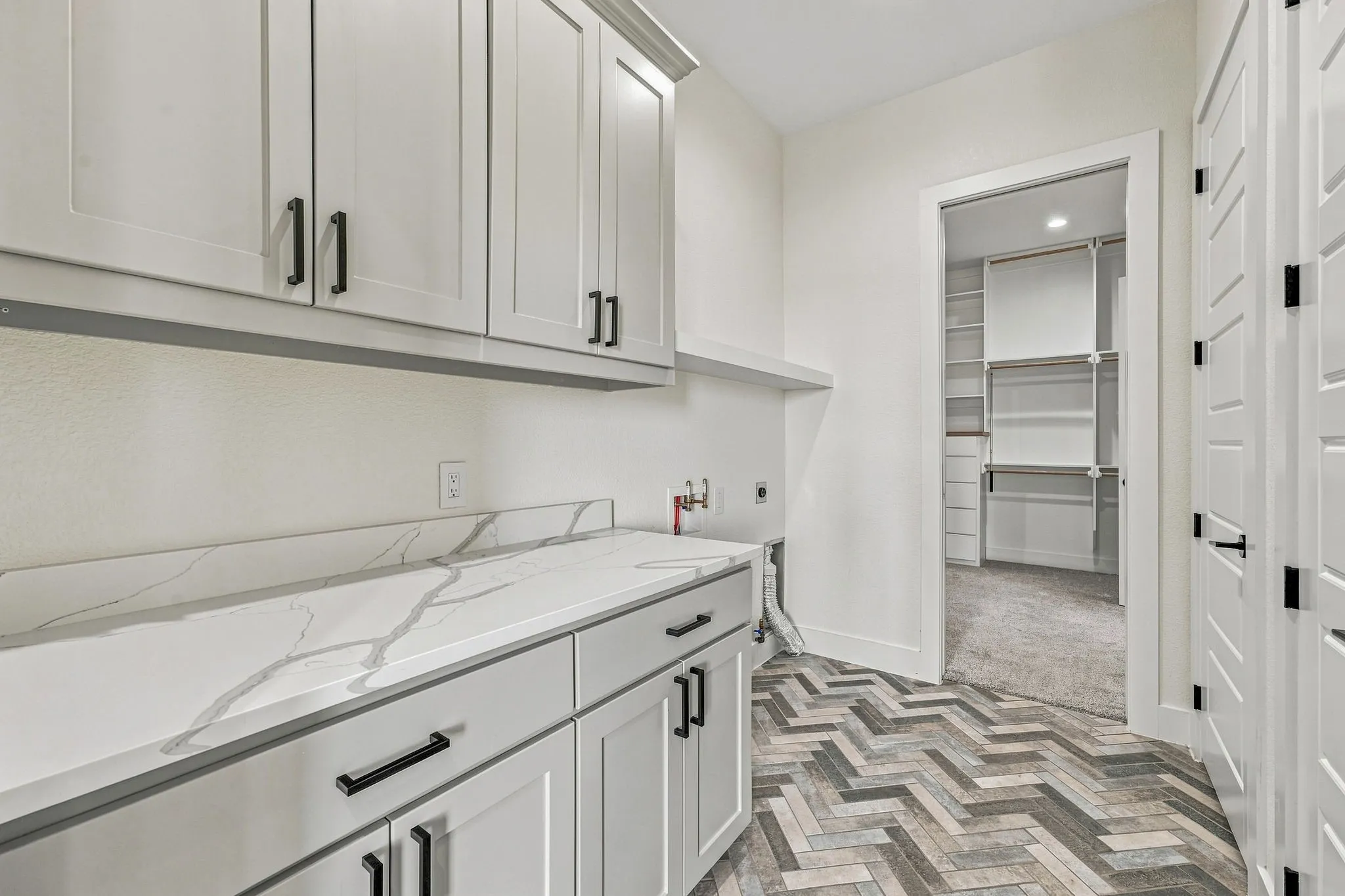Shaker-style cabinetry with matte black hardware, stone-finish countertops, wood-finish herringbone flooring, and custom closet shelving