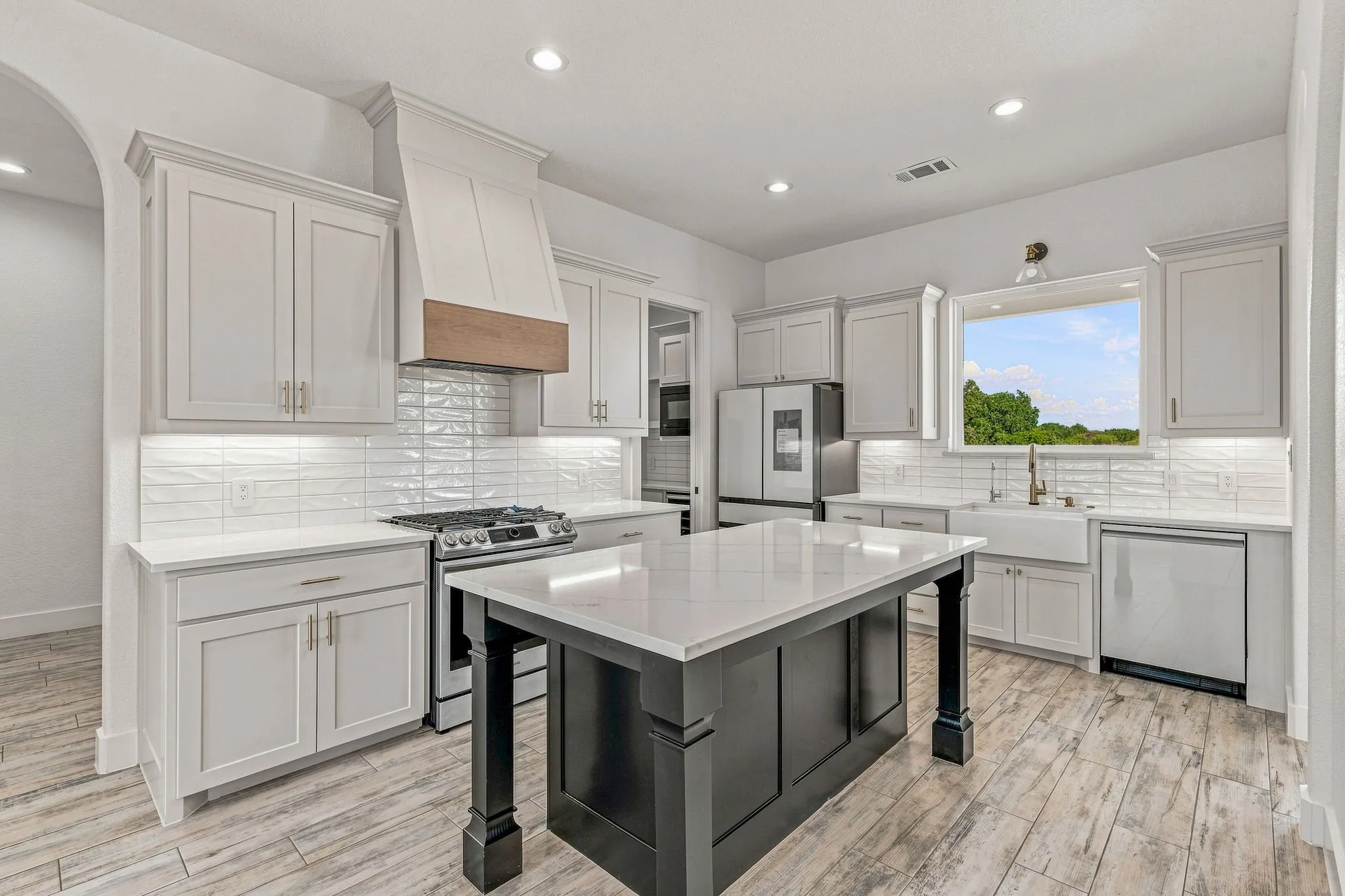 Kitchen featuring light cabinetry, a dark central island with a light countertop, stainless steel appliances, and a farmhouse sink