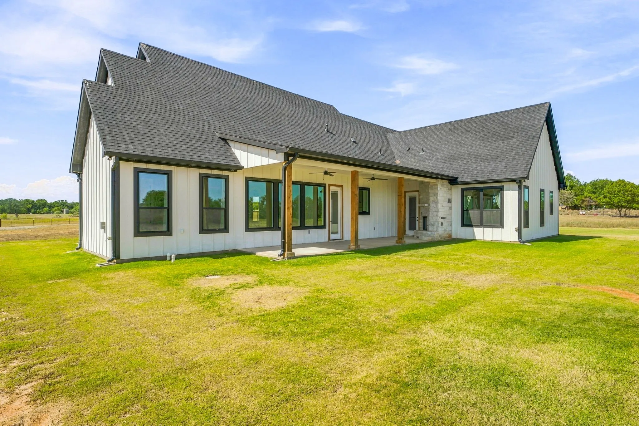 Contemporary farmhouse exterior featuring white board and batten siding, dark-framed windows, and a covered patio with exposed wood columns