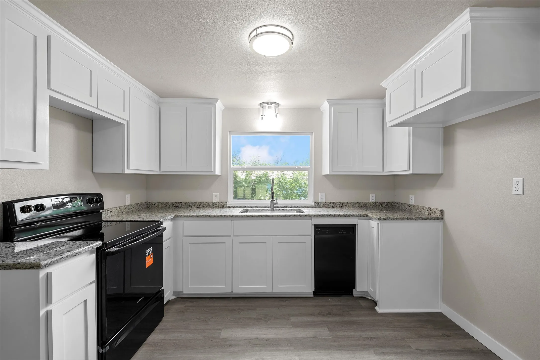 Kitchen featuring white shaker cabinetry, speckled countertops, stainless steel sink, black range, and wood-finish flooring