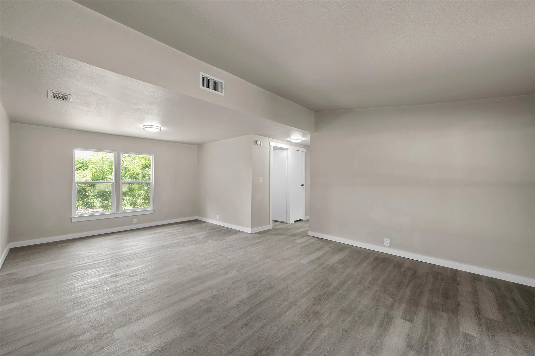 Spacious room featuring wood-finish flooring, light-colored walls, and a large window