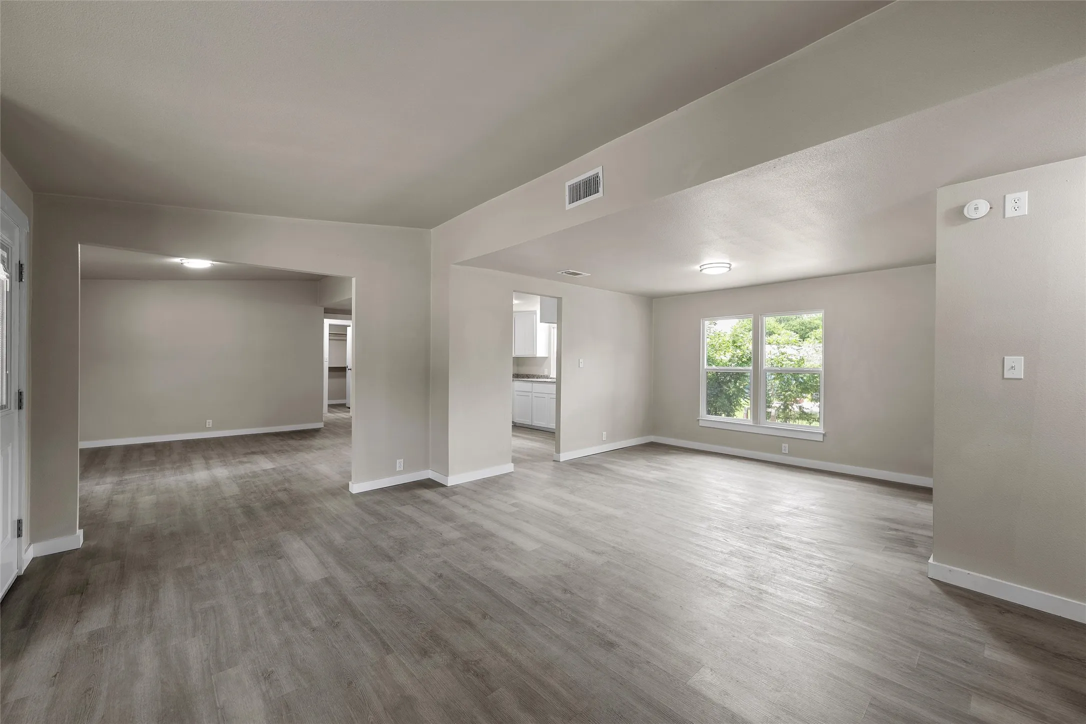 Open-concept living space featuring wood-finish flooring, recessed lighting, and a kitchen with white cabinetry, light-toned countertops, and a stainless steel sink