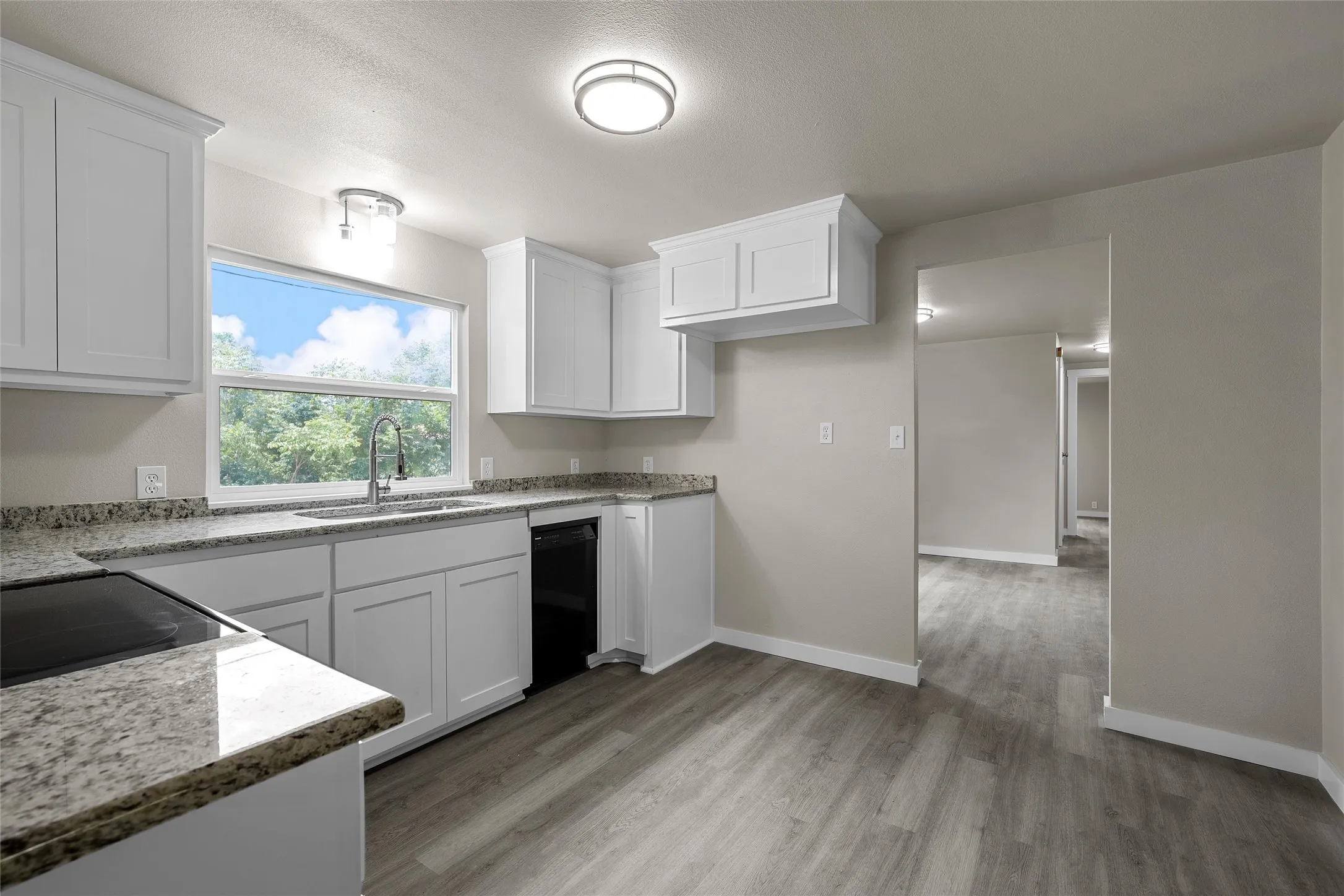 Kitchen featuring white shaker cabinetry, speckled countertops, stainless steel sink with gooseneck faucet, black built-in dishwasher, and wood-finish flooring