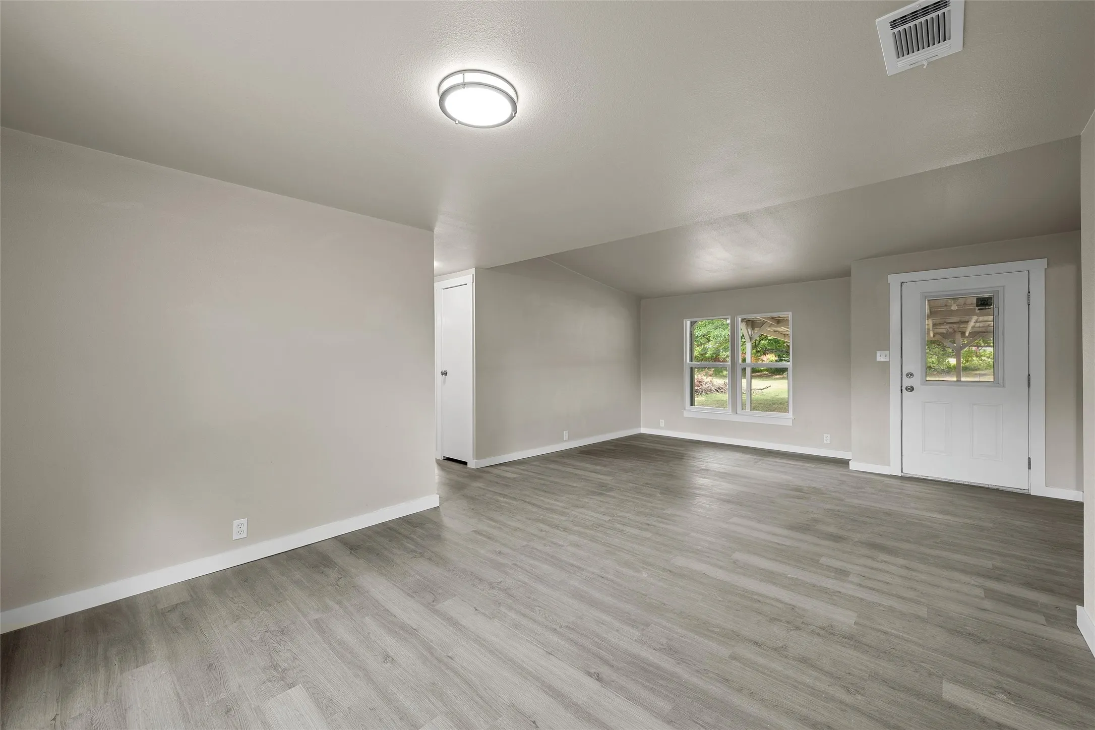 Open-concept living space featuring wood-finish flooring, recessed lighting, and a kitchen with white cabinetry, light-toned countertops, and a stainless steel sink