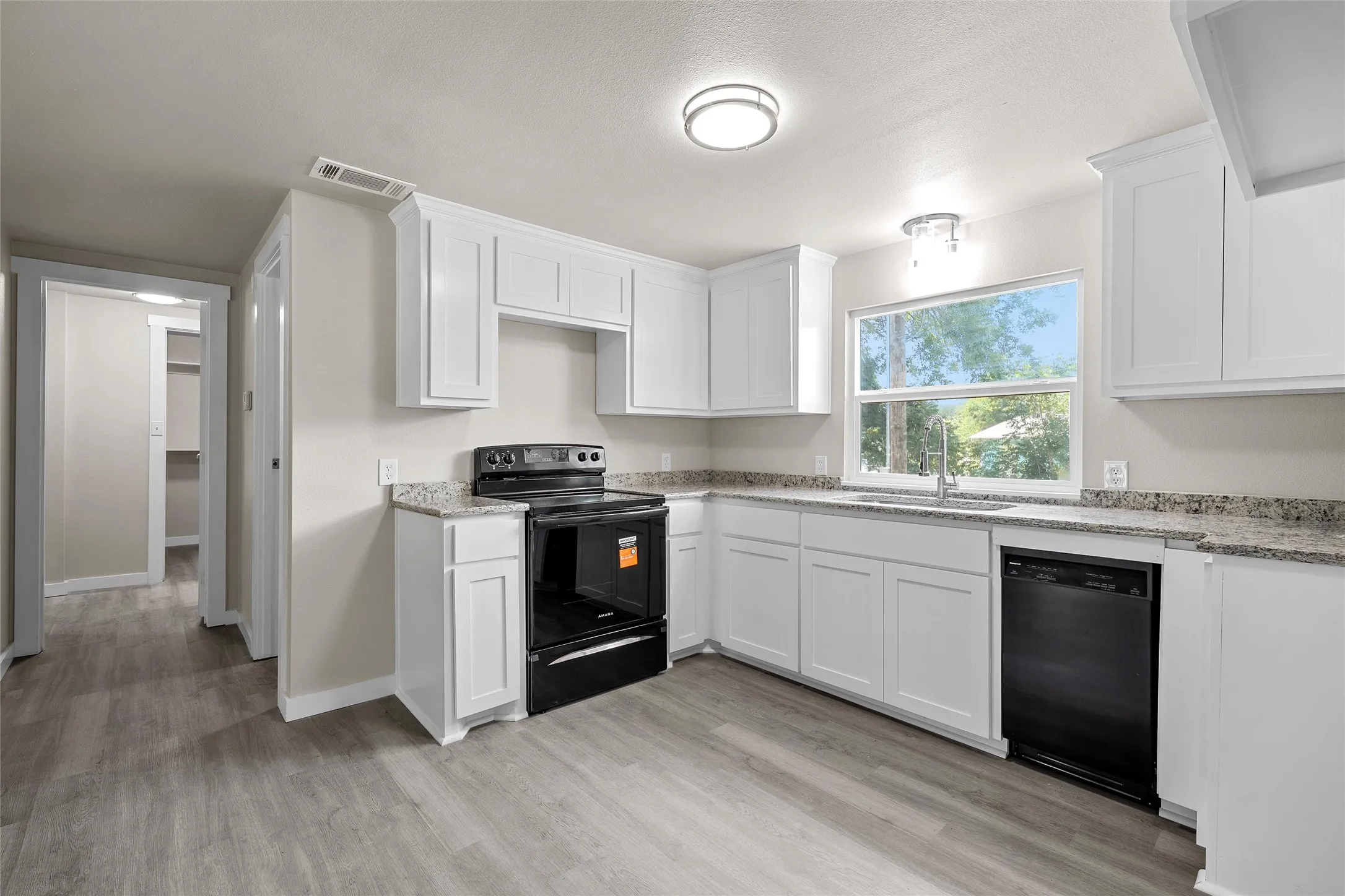 Kitchen featuring white cabinetry, wood-finish flooring, a window over the sink, stone countertops, and black appliances