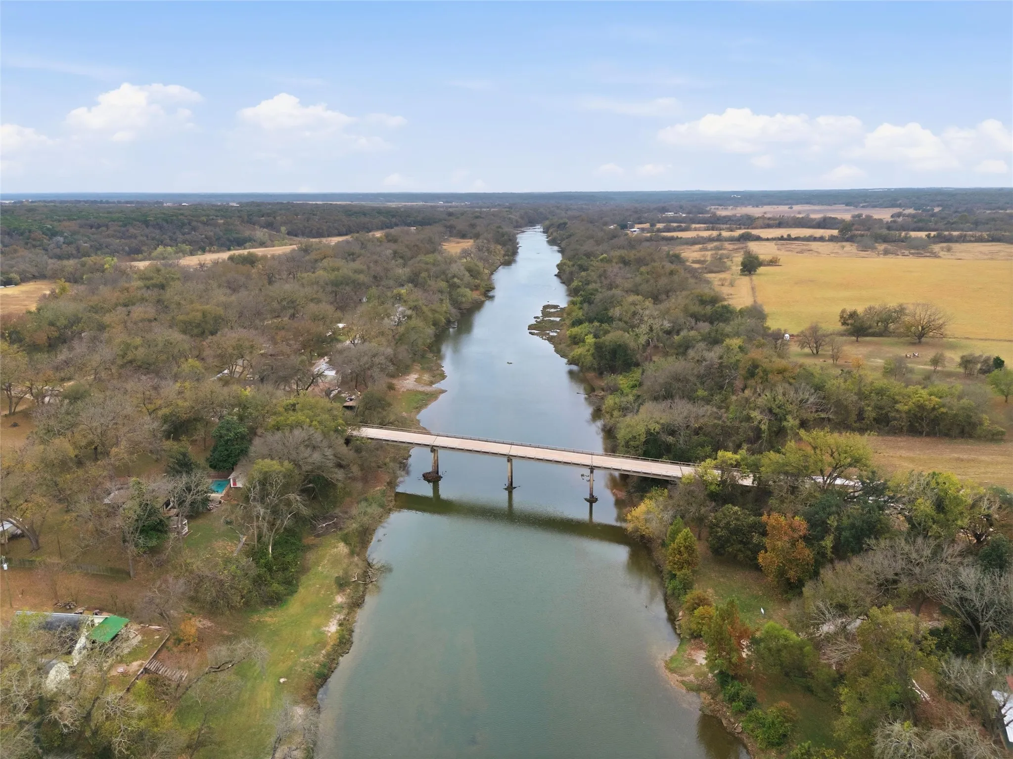 Riverfront property with bridge access, surrounded by mature trees and expansive open fields