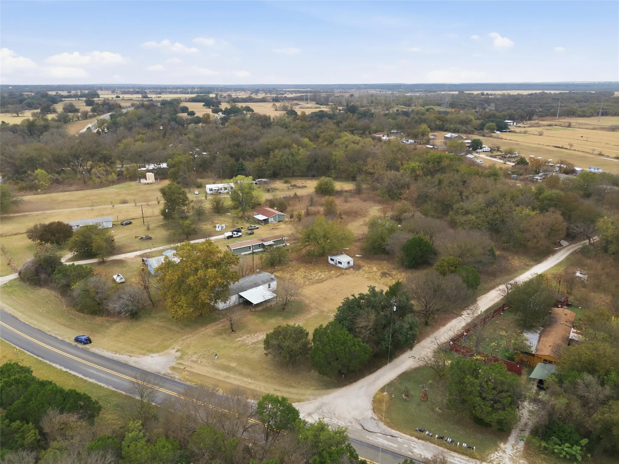 Expansive rural landscape featuring scattered residential structures, mature trees, and a paved road