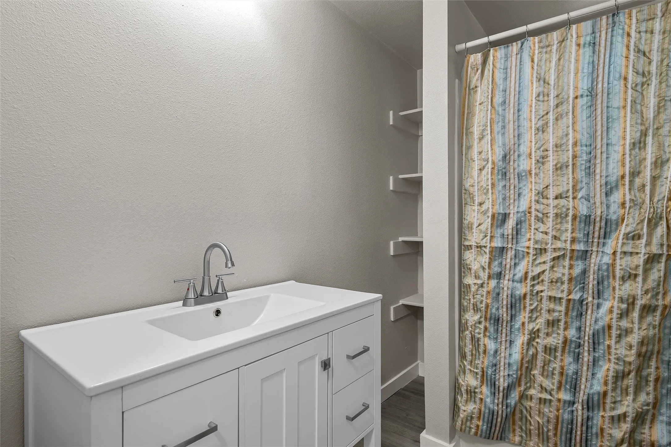 White vanity with integrated rectangular sink, chrome two-handle faucet, and built-in shelving