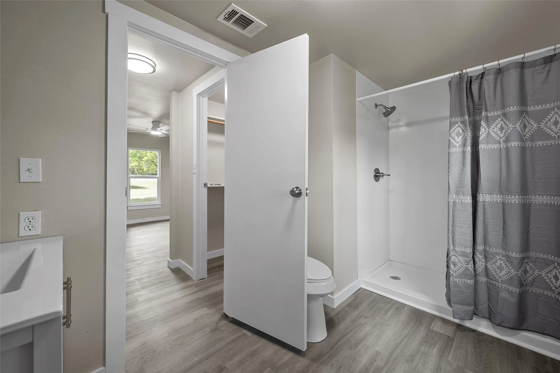 Wood-finish flooring, built-in shower with showerhead, toilet, vanity with sink, and white trim