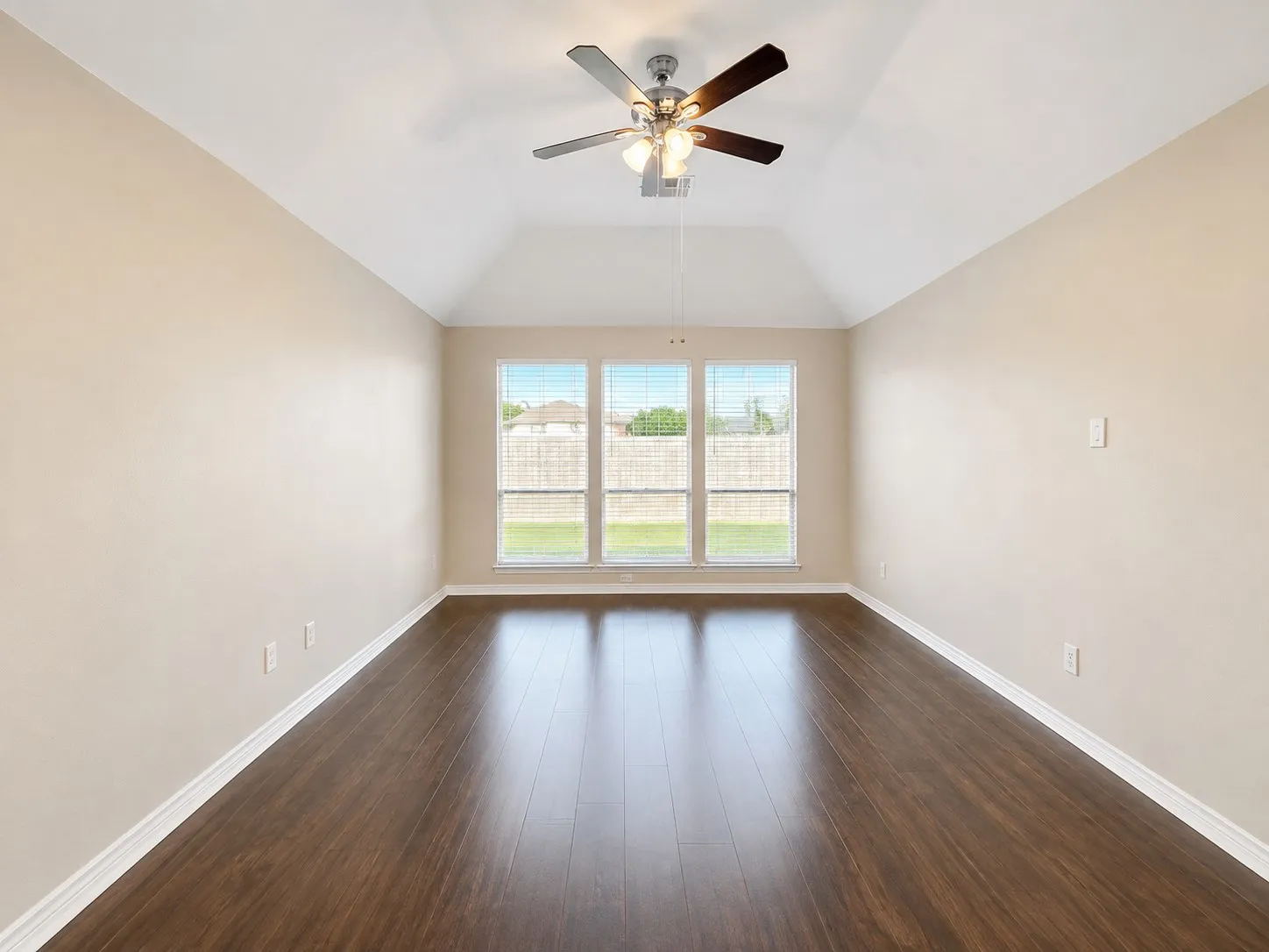 Vaulted ceiling with a ceiling fan, wood-finish flooring, three windows with blinds, and neutral wall paint