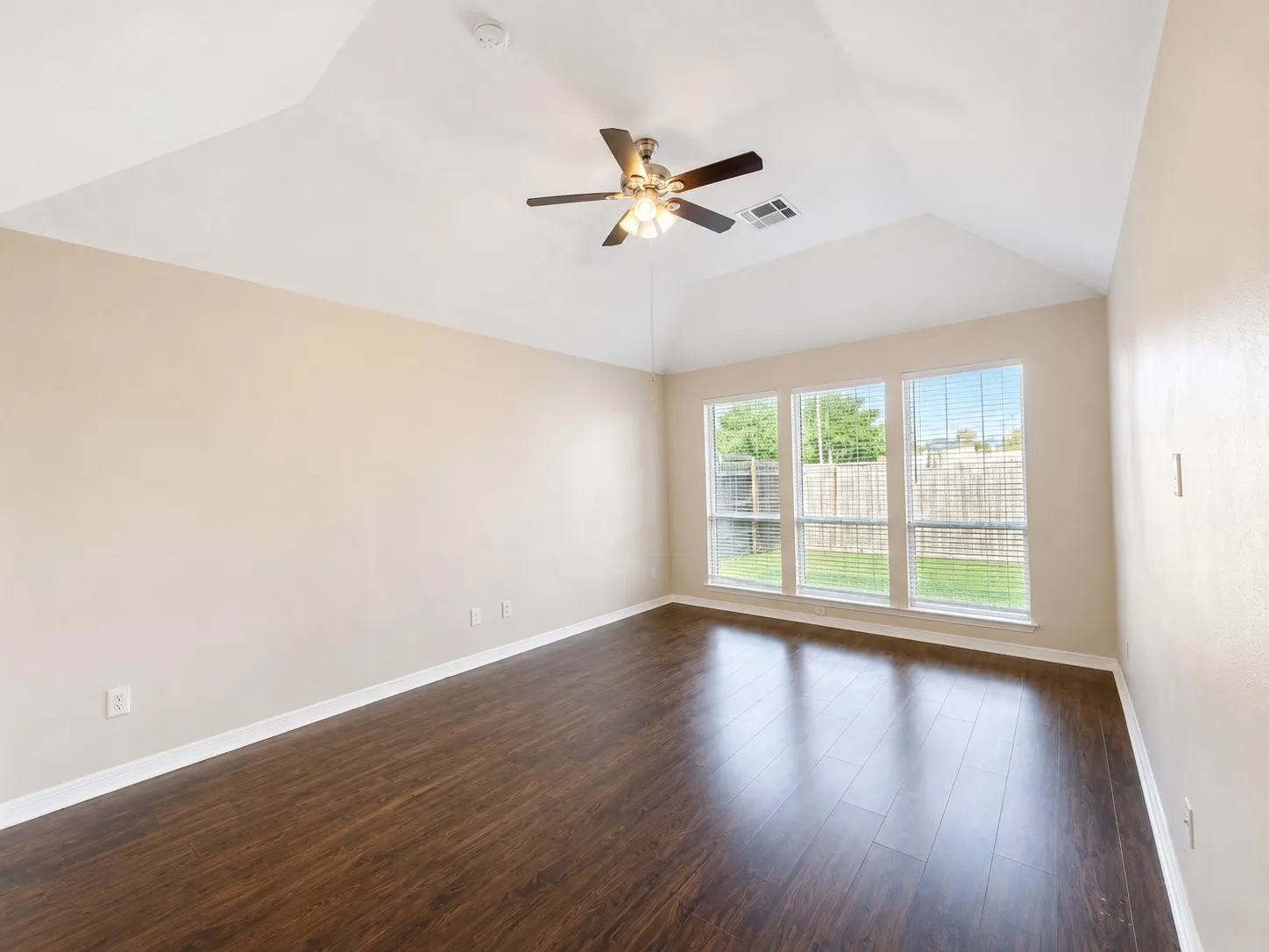 Vaulted ceiling with a ceiling fan light fixture, wood-finish flooring, three transom windows, and white trim