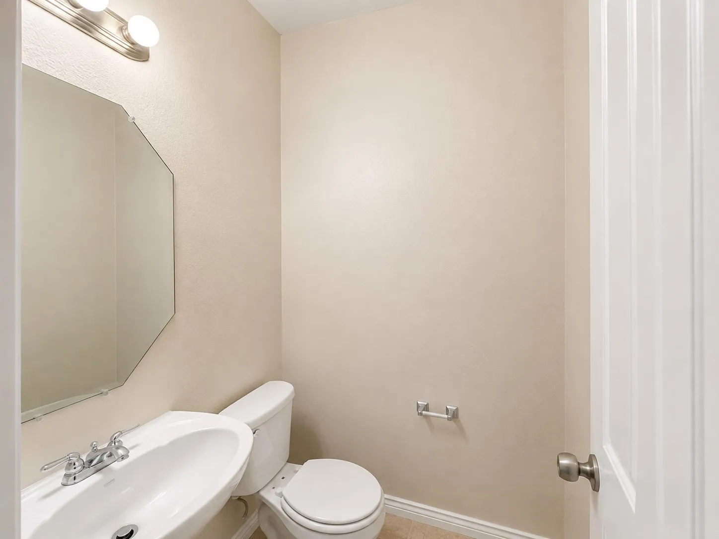 Pedestal sink with chrome faucet, octagonal wall mirror, and vanity lighting