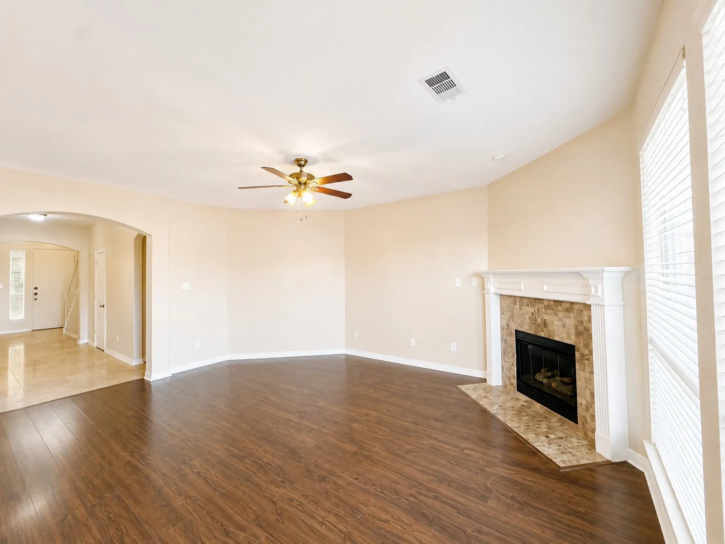 Wood-finish flooring, tiled fireplace with mantel, ceiling fan, arched doorway, and bay windows