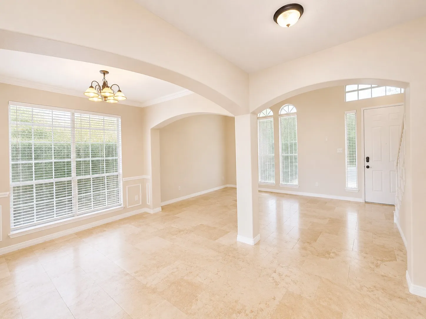 Expansive tile flooring, multiple arched doorways, large window with blinds, decorative wainscoting, and a multi-pane front door