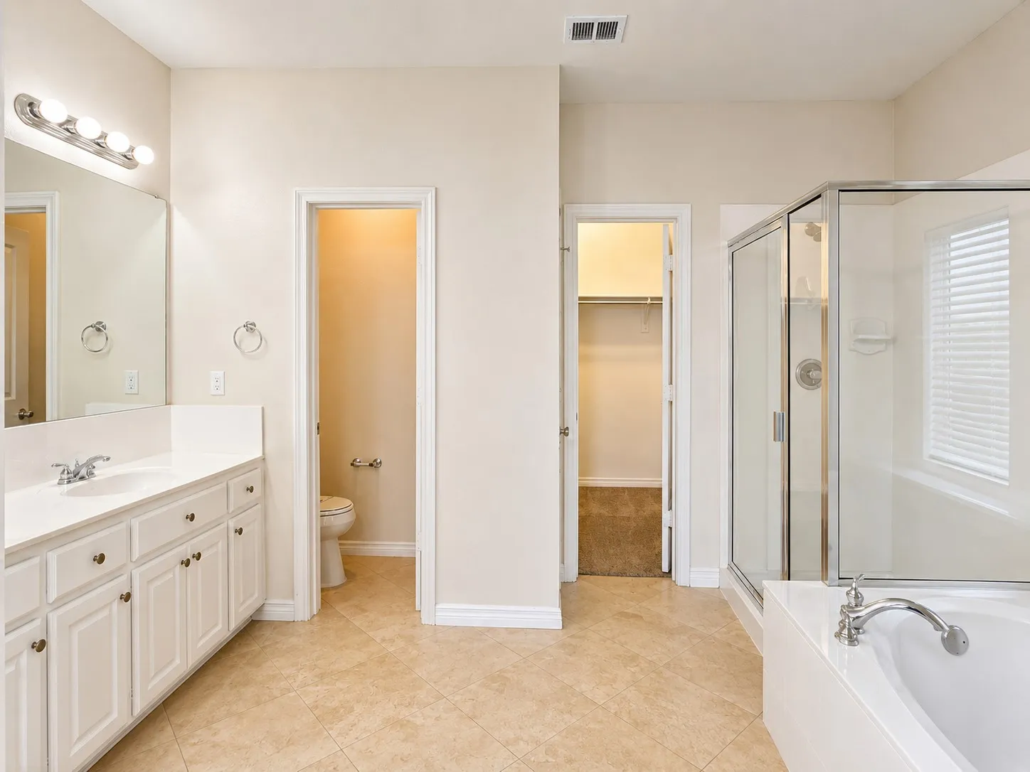 Neutral-toned tile flooring, large vanity with white cabinetry and countertop, mirrored wall, glass-enclosed shower, and a built-in bathtub