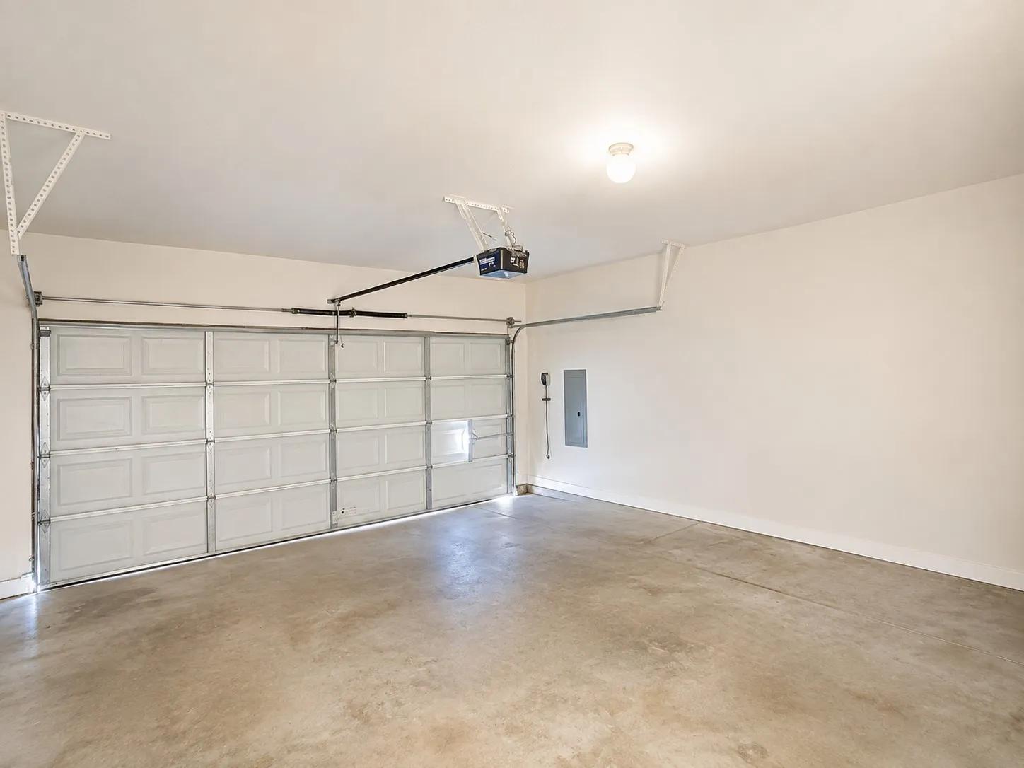 Spacious garage featuring a concrete floor, painted walls, overhead lighting, and an automatic garage door opener