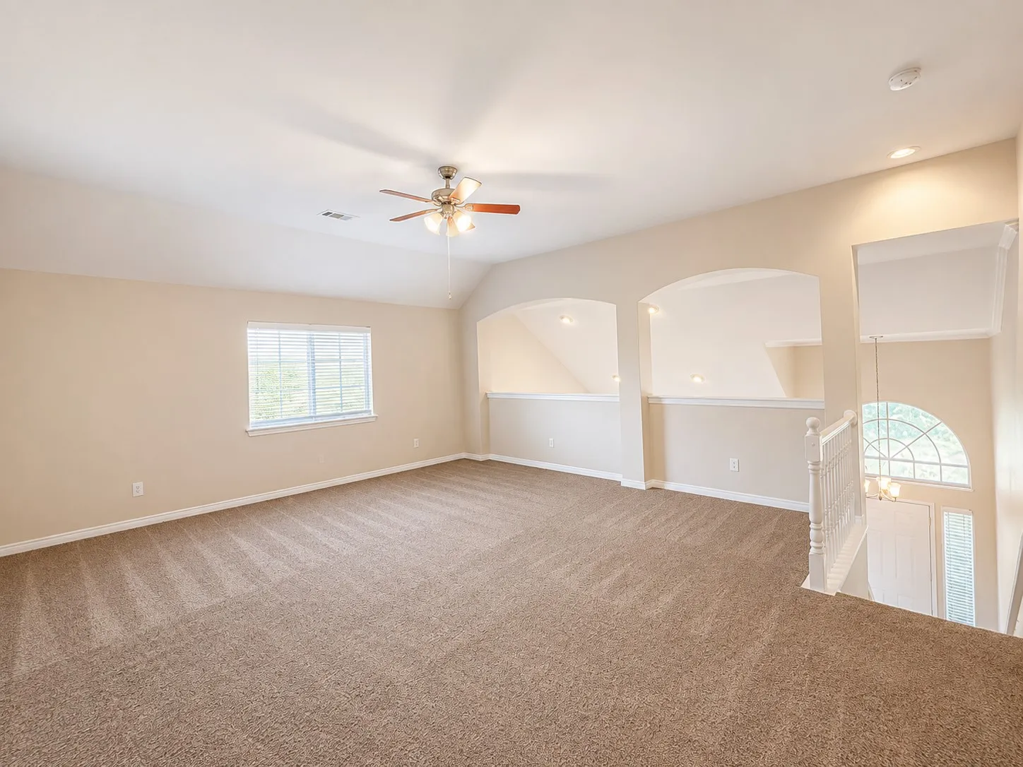 Expansive carpeted loft with an arched window, ceiling fan, and recessed lighting