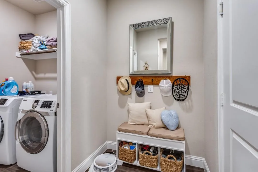 Laundry area with built-in shelving, wood-finish flooring, and a dedicated storage bench with a wood-tone coat rack