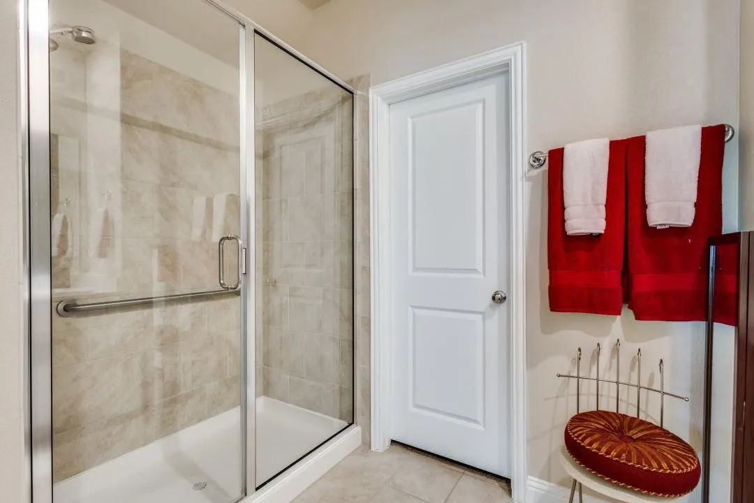 Glass-enclosed shower with ceramic tile surround, white shower pan, and a grab bar
