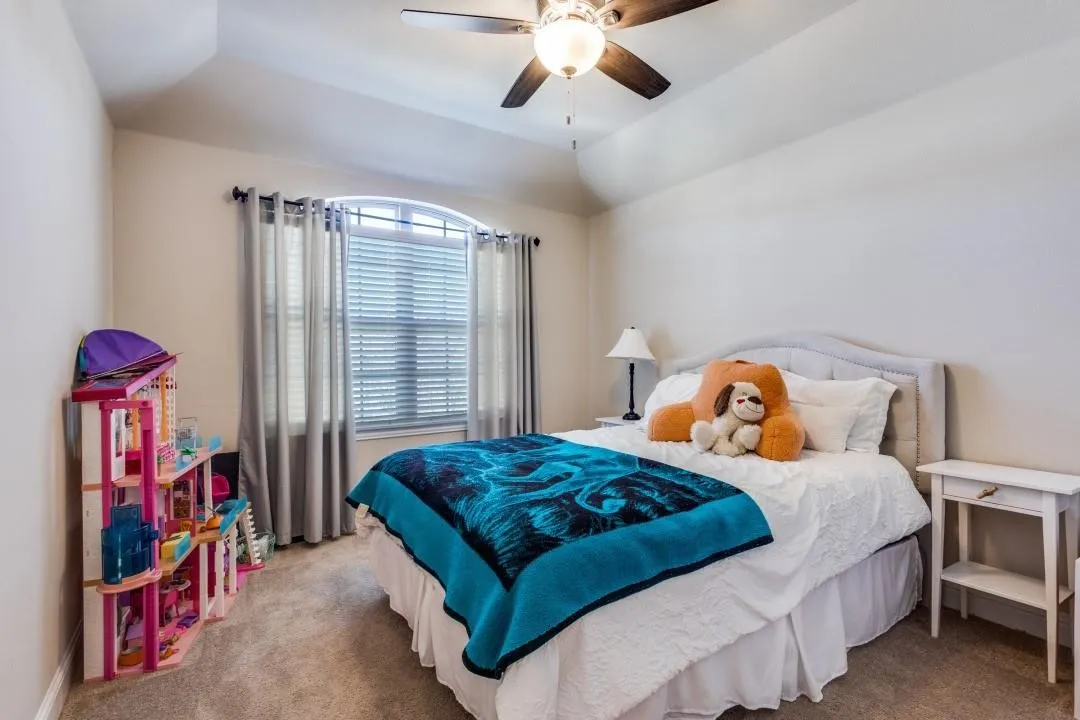 Arch-top window with blinds, ceiling fan with integrated lighting, carpeted flooring, tray ceiling, and upholstered headboard