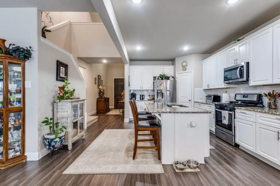 Open-concept kitchen featuring white shaker cabinetry, stainless steel appliances, granite countertops, and a kitchen island with seating