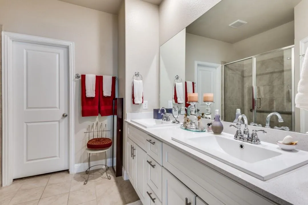 Dual vanity with integrated sinks, white cabinetry, chrome fixtures, and a glass-enclosed shower