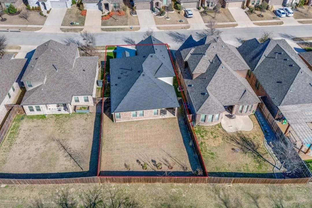 Aerial perspective showcasing a single-family residence with a dark shingle roof, brick and siding exterior, and a fenced backyard