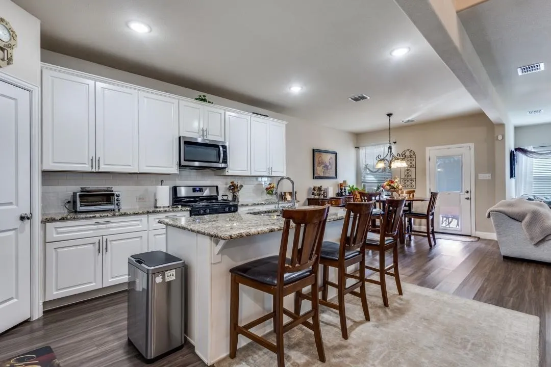 Kitchen featuring white cabinetry, stainless steel appliances, granite countertops, and wood-finish flooring