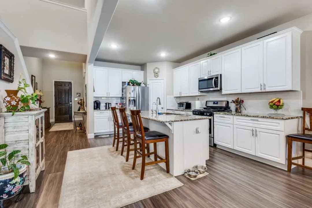 Kitchen featuring white cabinetry, granite countertops, stainless steel appliances, a kitchen island, and wood-finish flooring