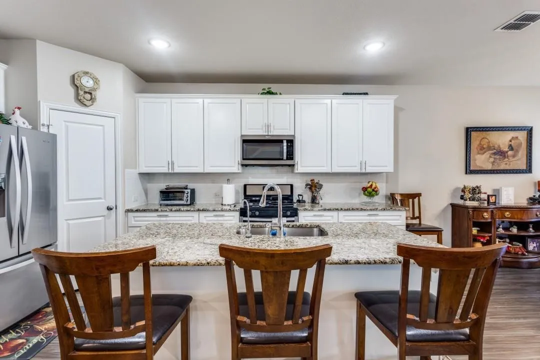 Kitchen featuring white cabinetry, granite countertops, stainless steel appliances, a tile backsplash, and wood-finish flooring