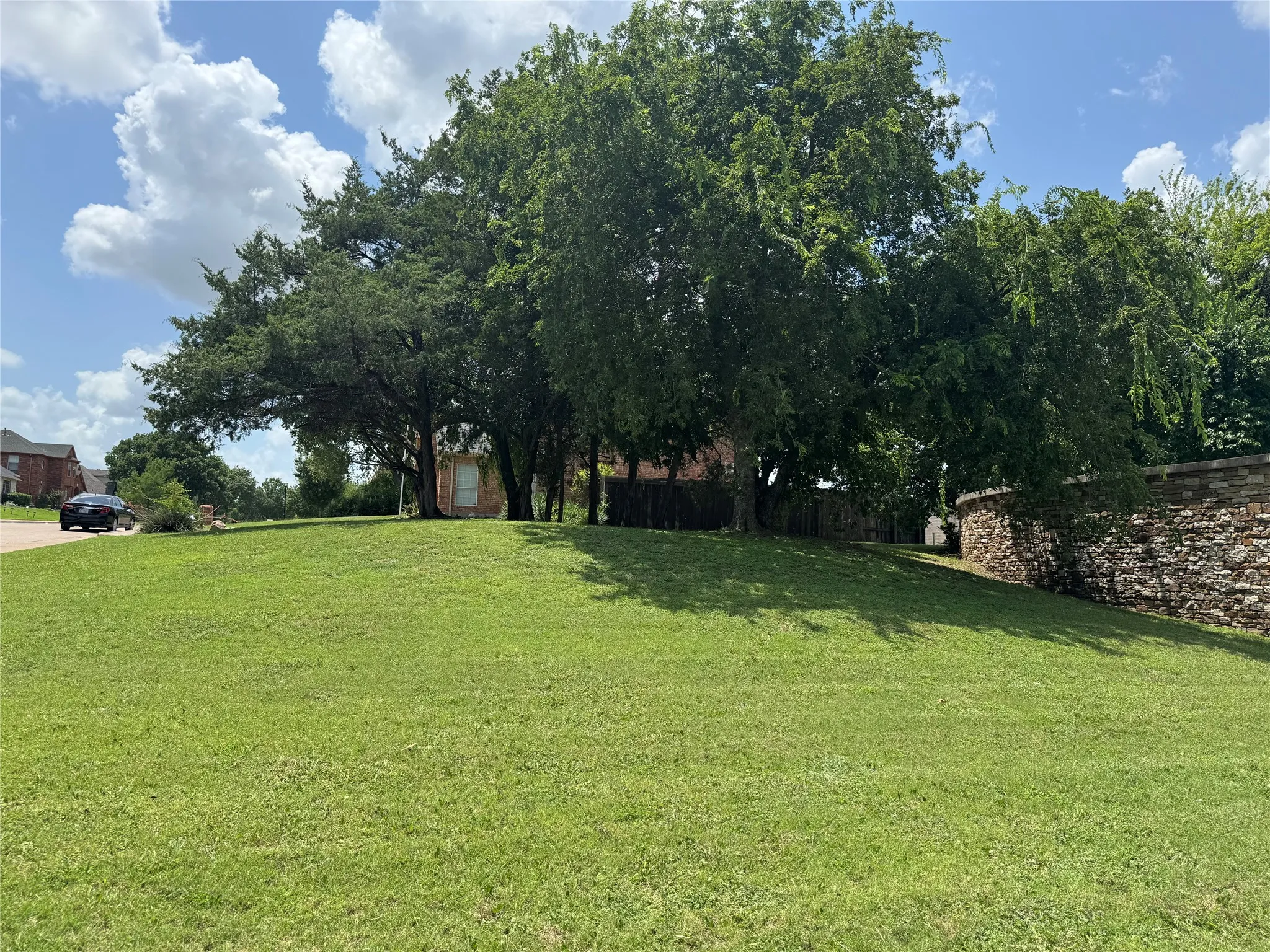 Expansive lawn with mature trees, offering a stone-clad retaining wall and surrounding residential architecture