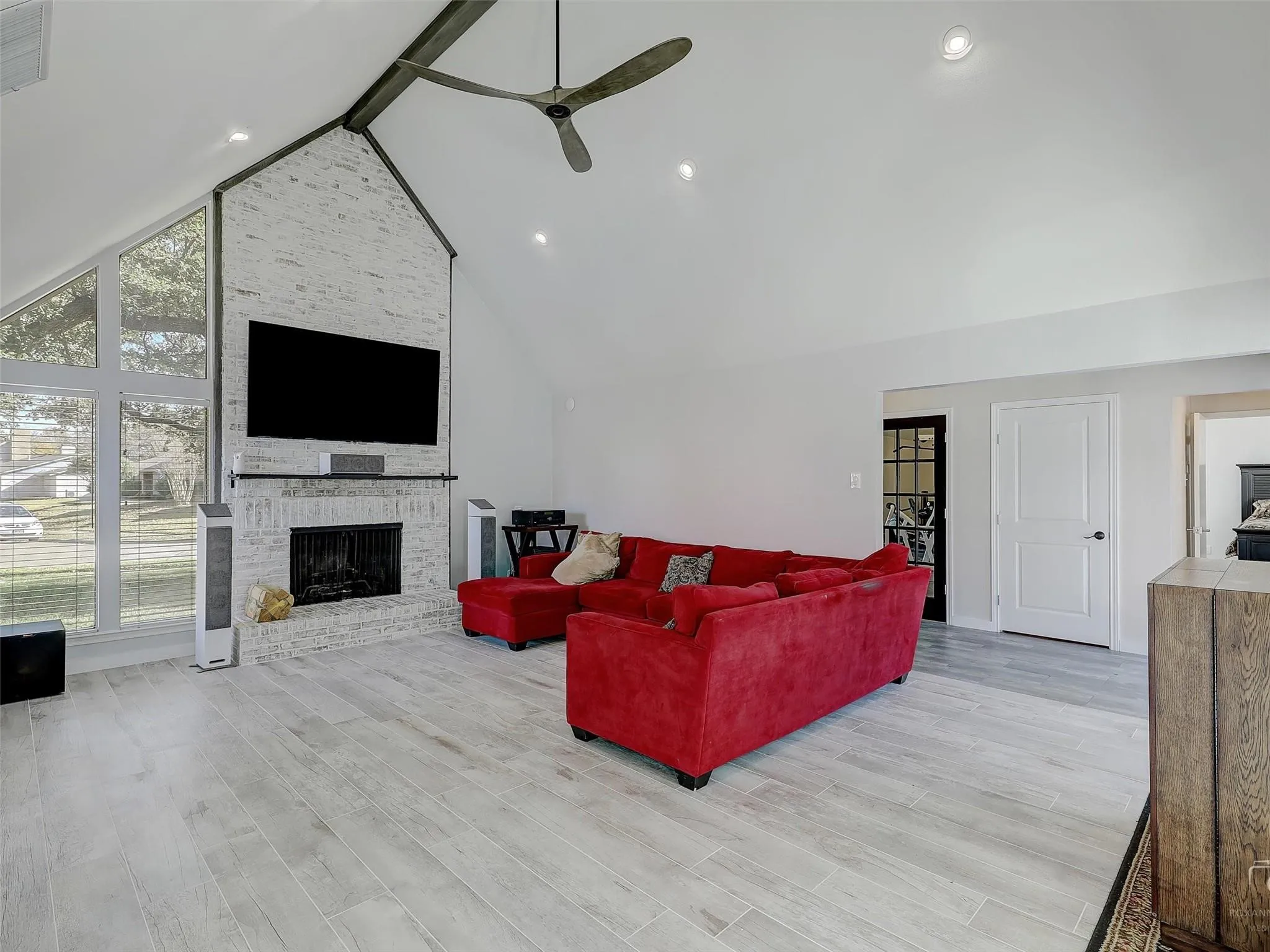 Living room with high vaulted ceiling, ceiling fan, light hardwood / wood-style floors, beam ceiling, and a fireplace
